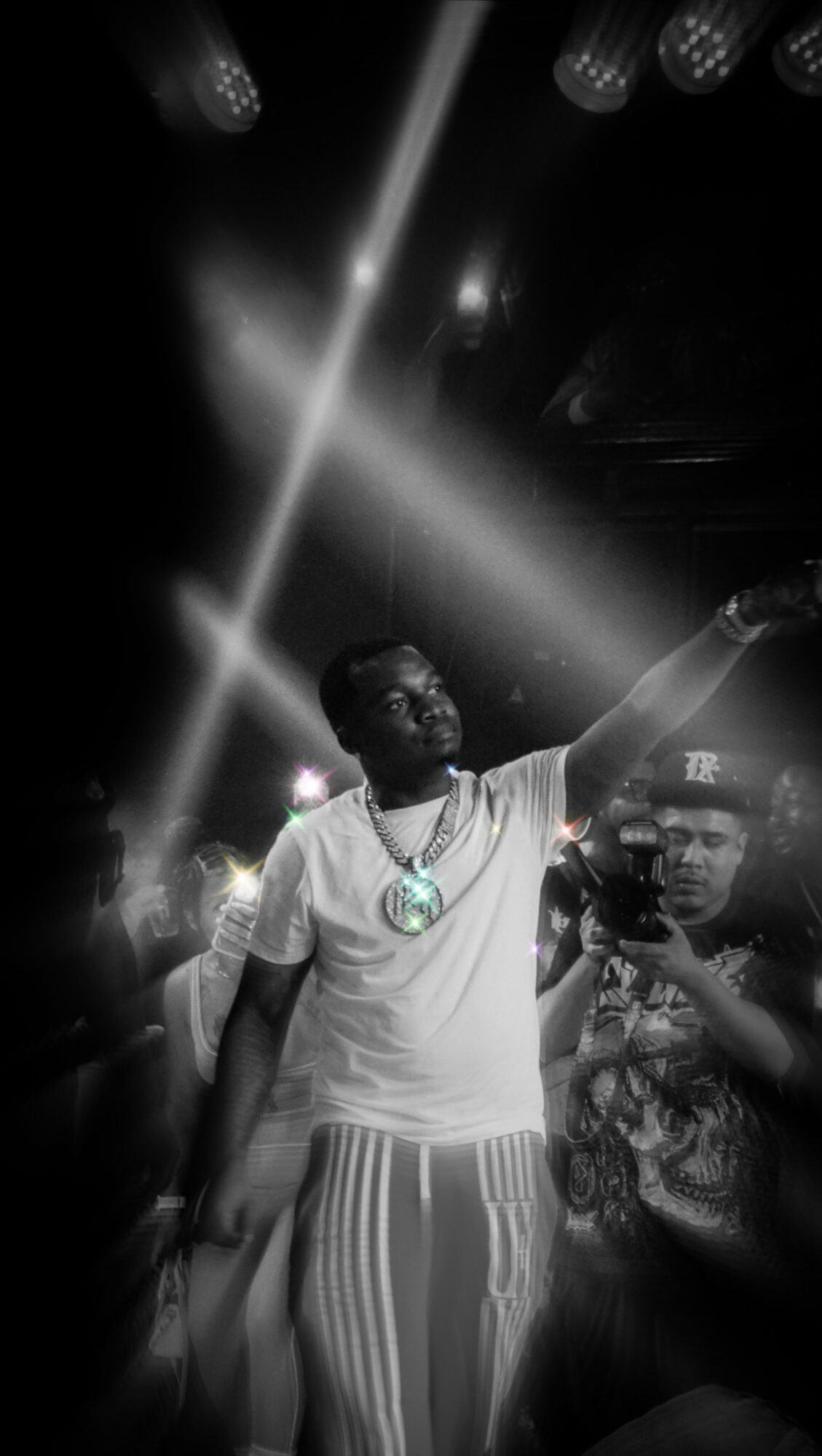 Person in white shirt and striped pants pointing upward in a dark, illuminated environment.