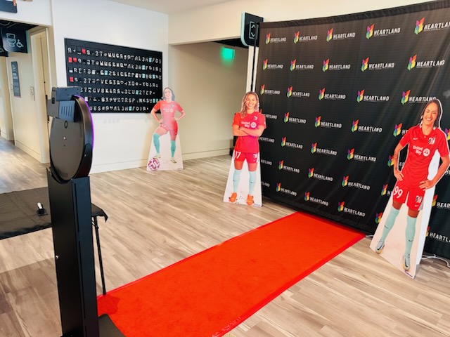 Red carpet on wooden floor with sports team cutouts and a black backdrop with logos.