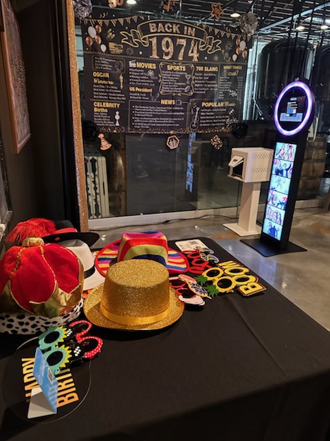 Table with colorful hats, a gold hat, and various accessories in front of a glass window with a poster about 1974.