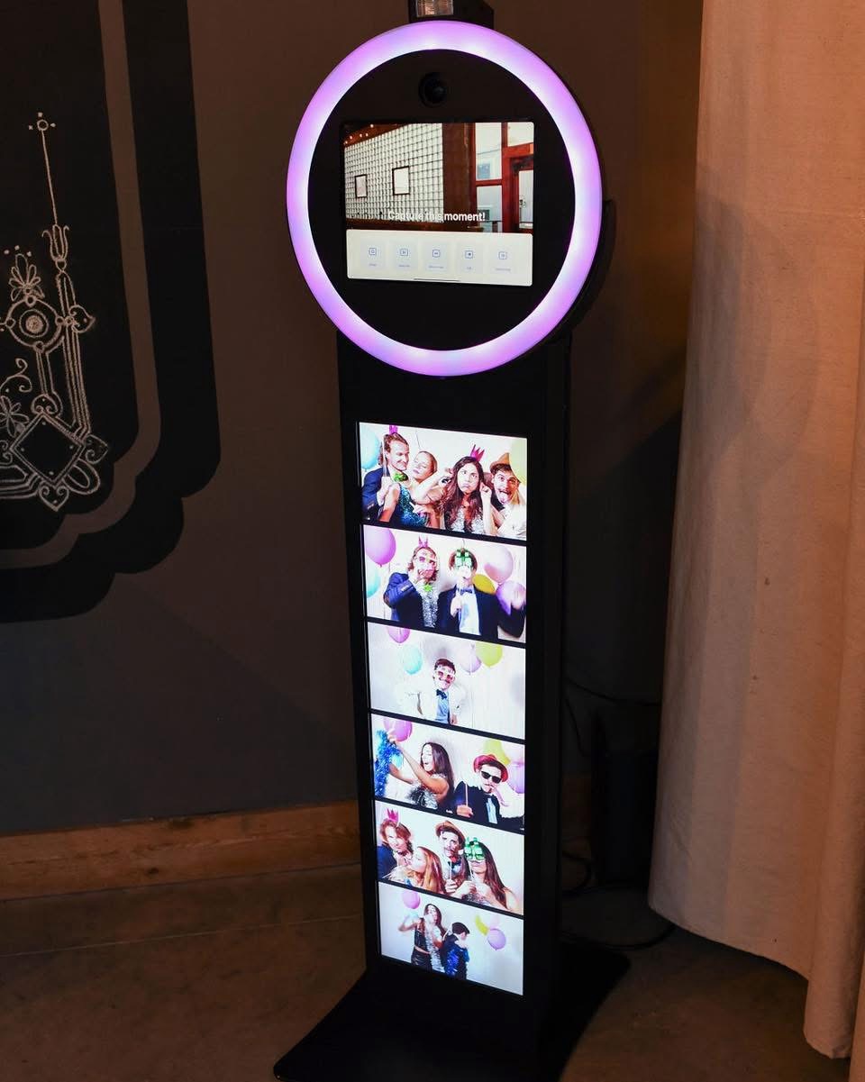 A digital photo booth with a circular light at the top and a screen displaying multiple group photos.