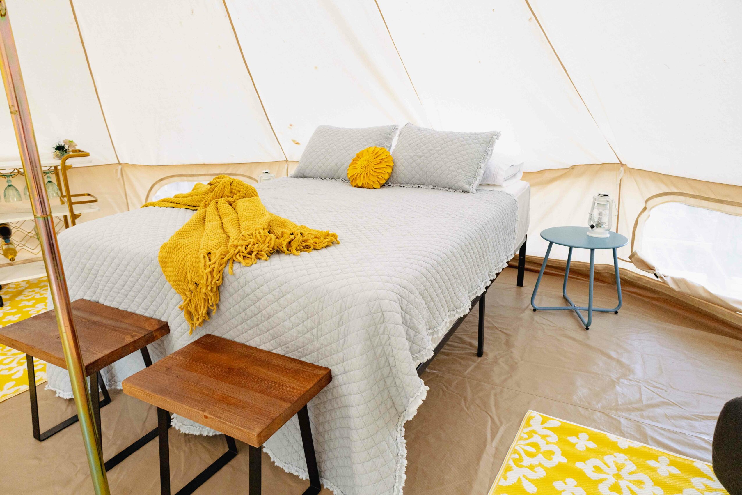 Bedroom with bed, pillows, yellow blanket, side table, and yellow and white rug.