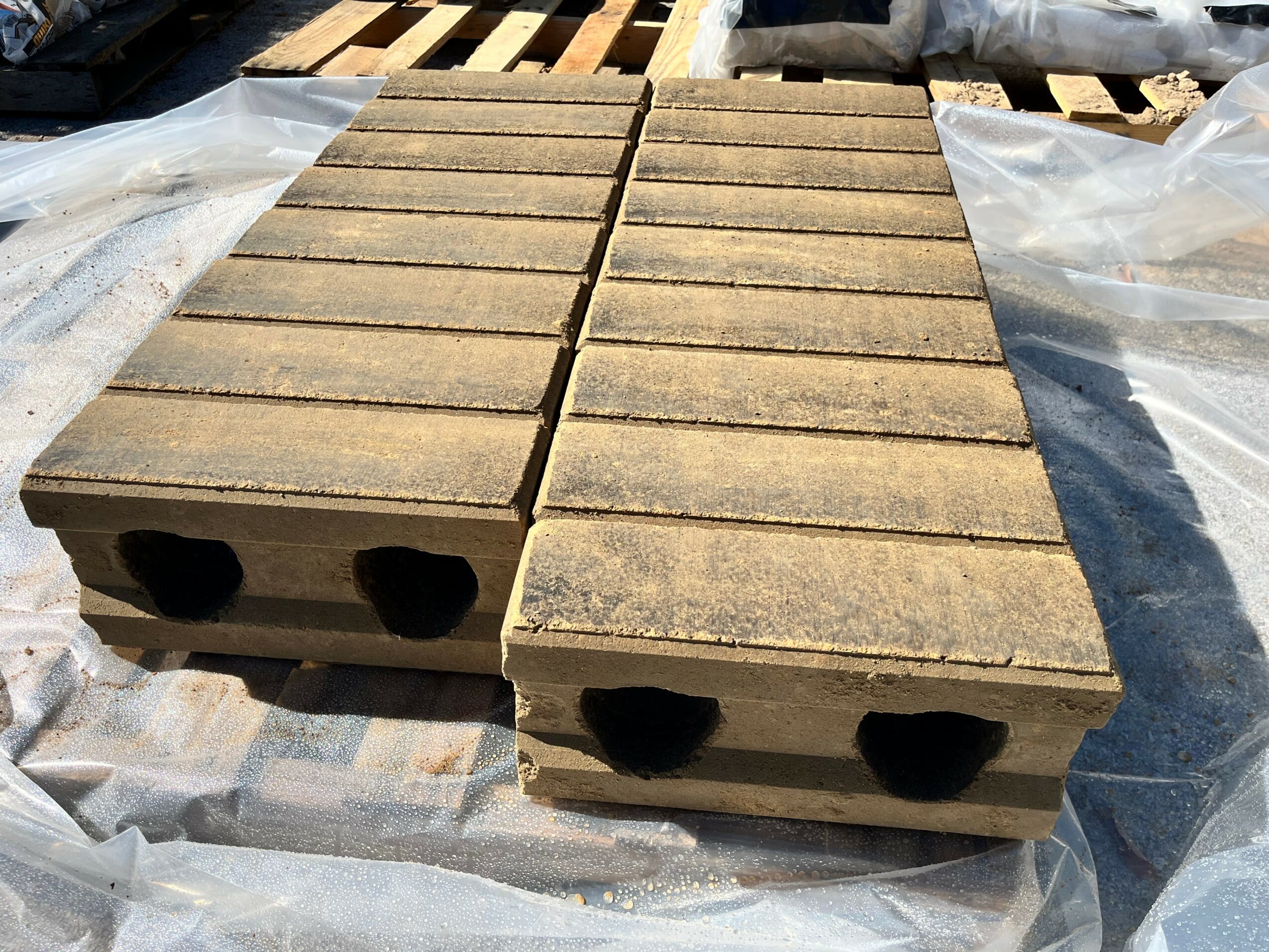 Stacked concrete blocks with hollow centers, arranged on a plastic sheet outdoors.