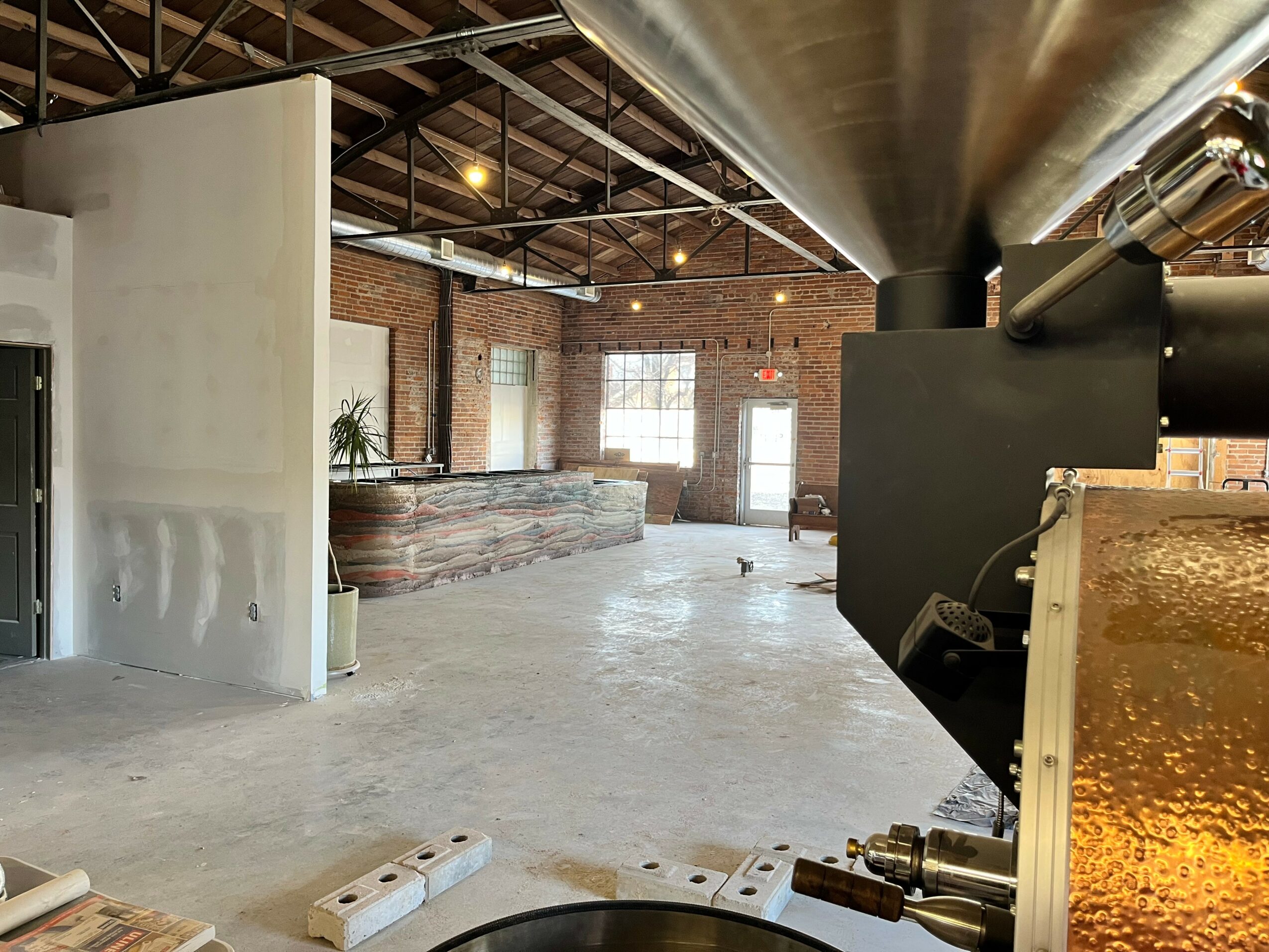 Industrial-style interior with brick walls, large windows, and exposed ceiling beams, featuring a reception desk and open space.