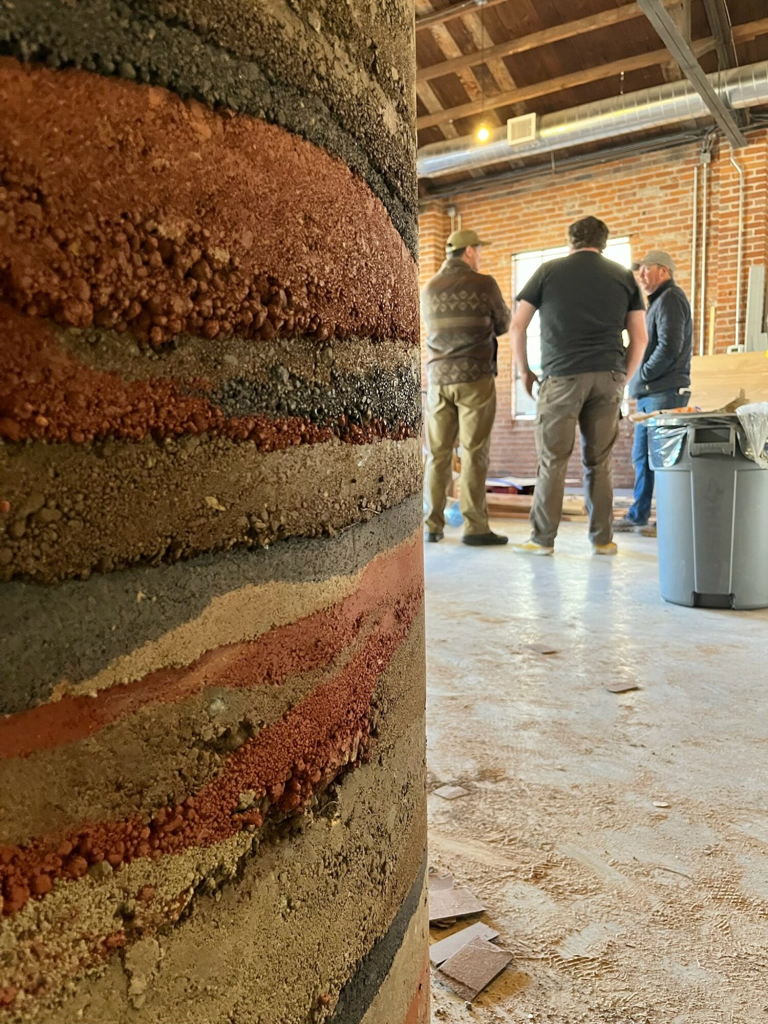 Close-up of a brick wall with three people standing and talking in an industrial space.