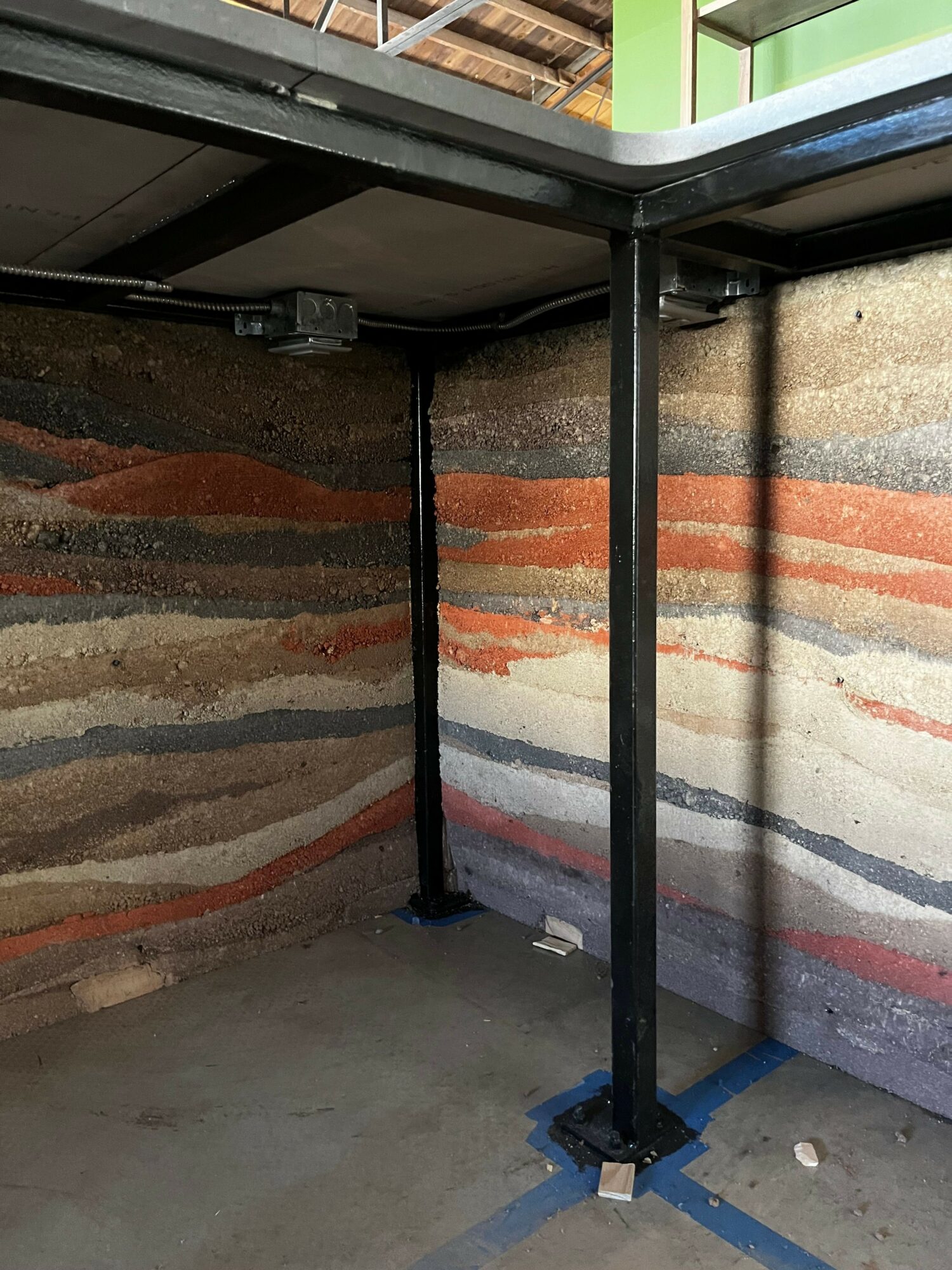 Interior corner with colorful layered stone wall, black metal support beams, and concrete floor.