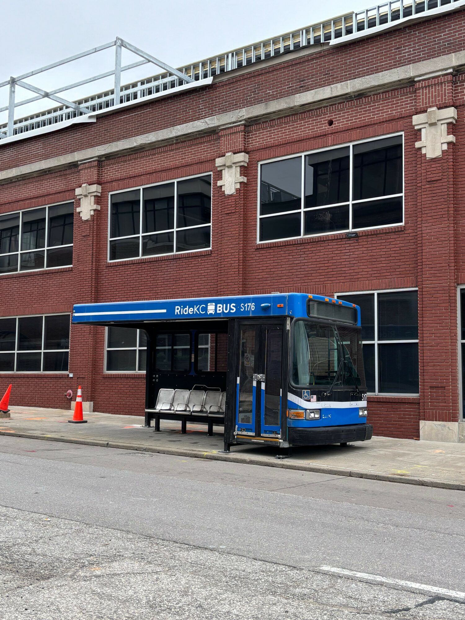 Blue bus parked on street in front of a red brick building with large windows.