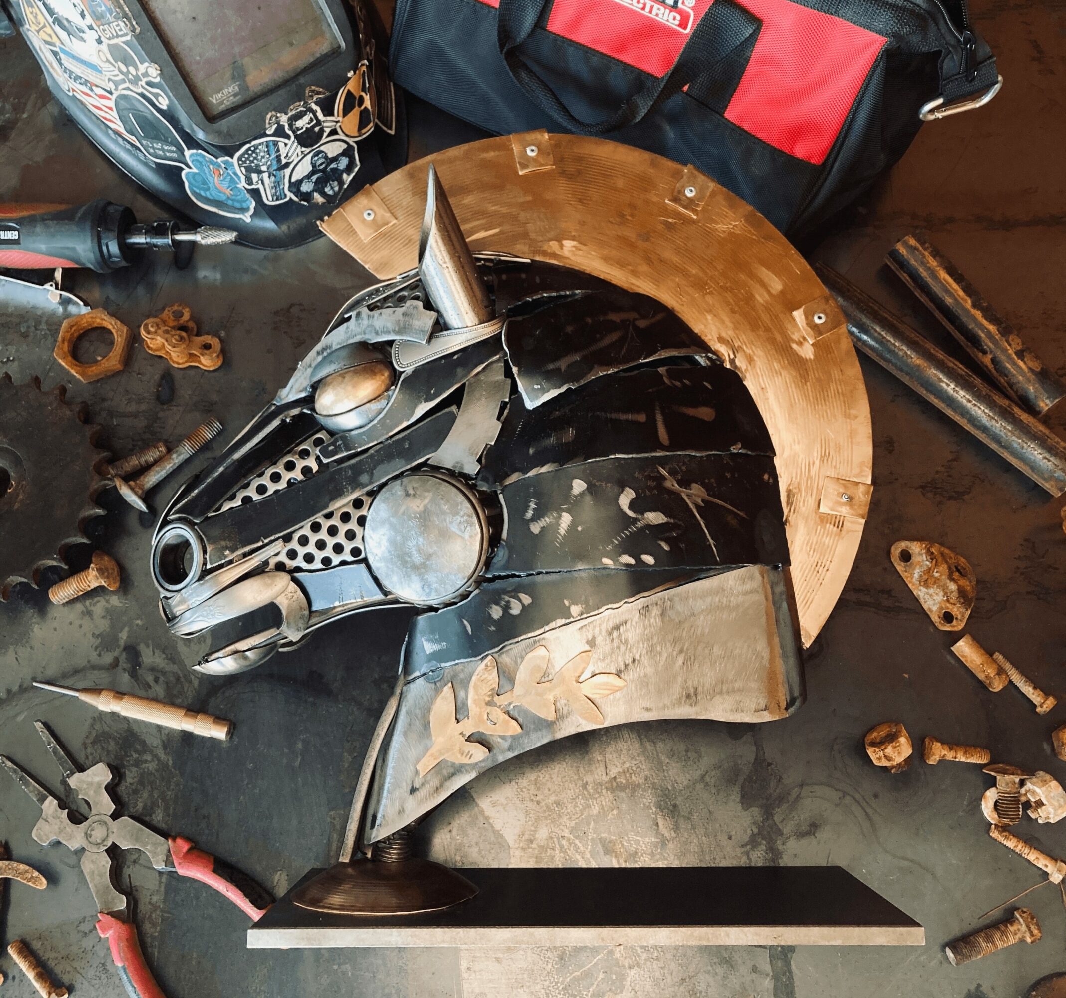 Workstation with welding helmet, toolbox, welding helmet, and various tools on a black surface.