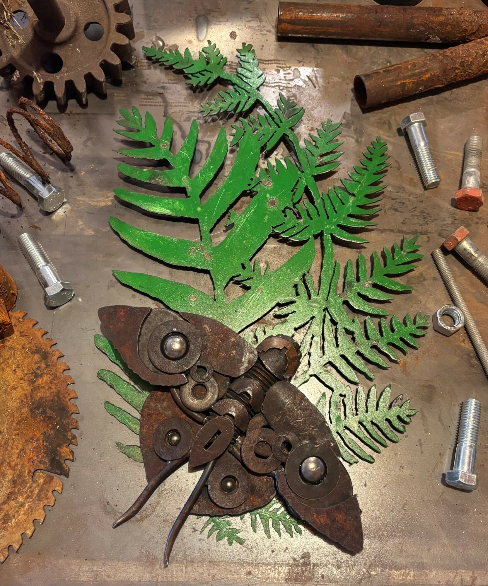 Metal tools and gears arranged on a wooden surface with green fern leaves.