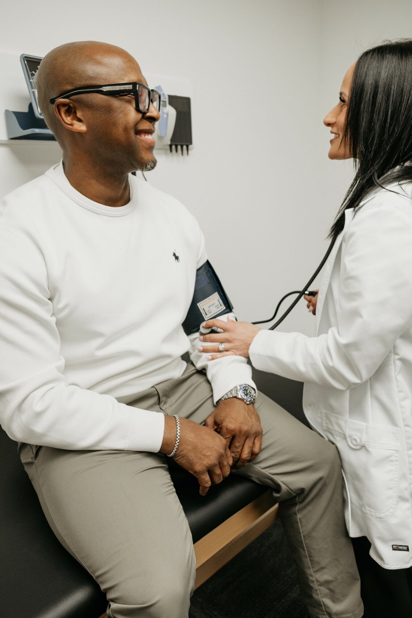 Doctor taking blood pressure of a smiling male patient in a clinical setting.
