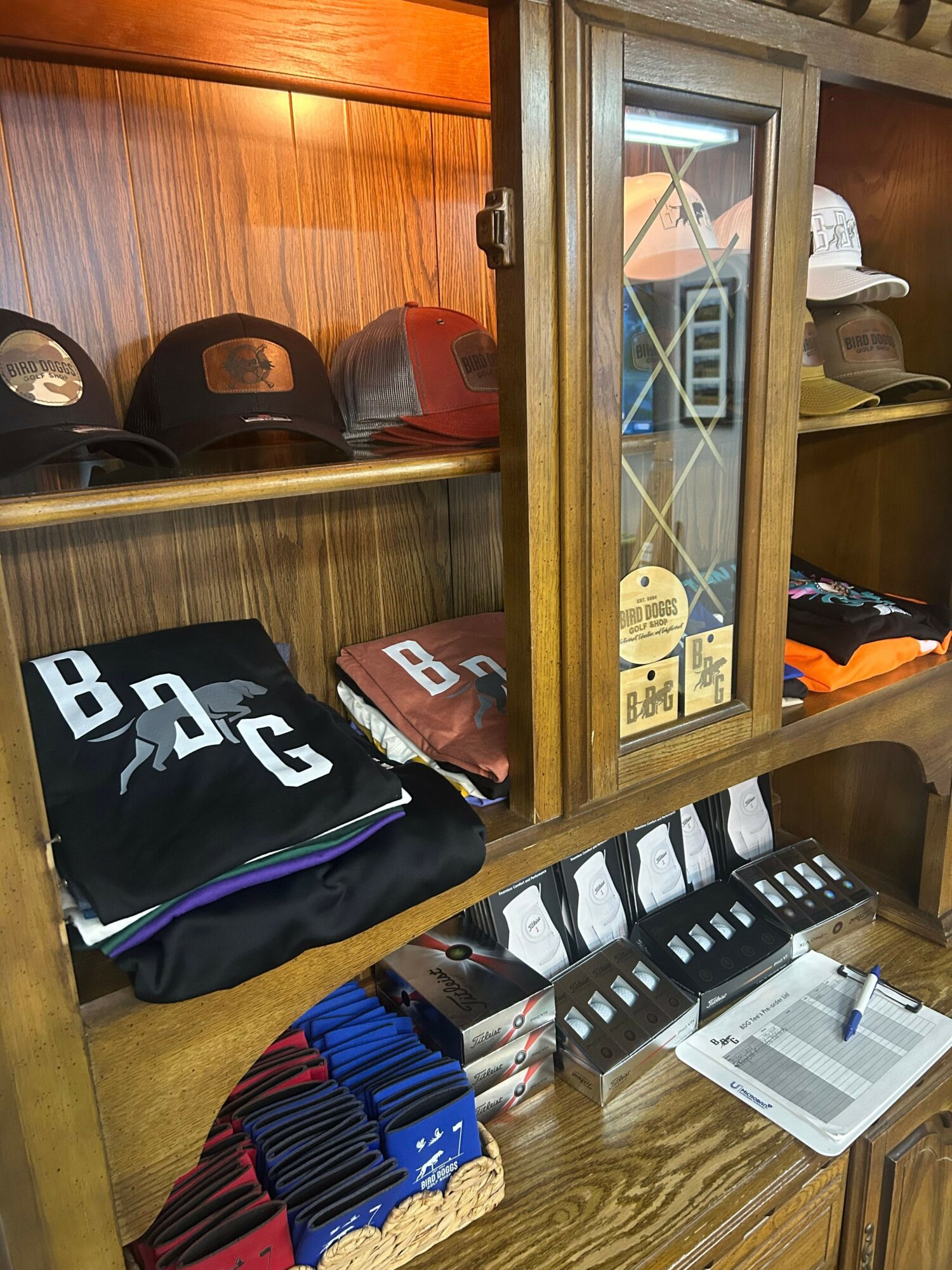 Wooden display cabinet with hats, folded clothing, and boxes inside, with a glass door and shelves.