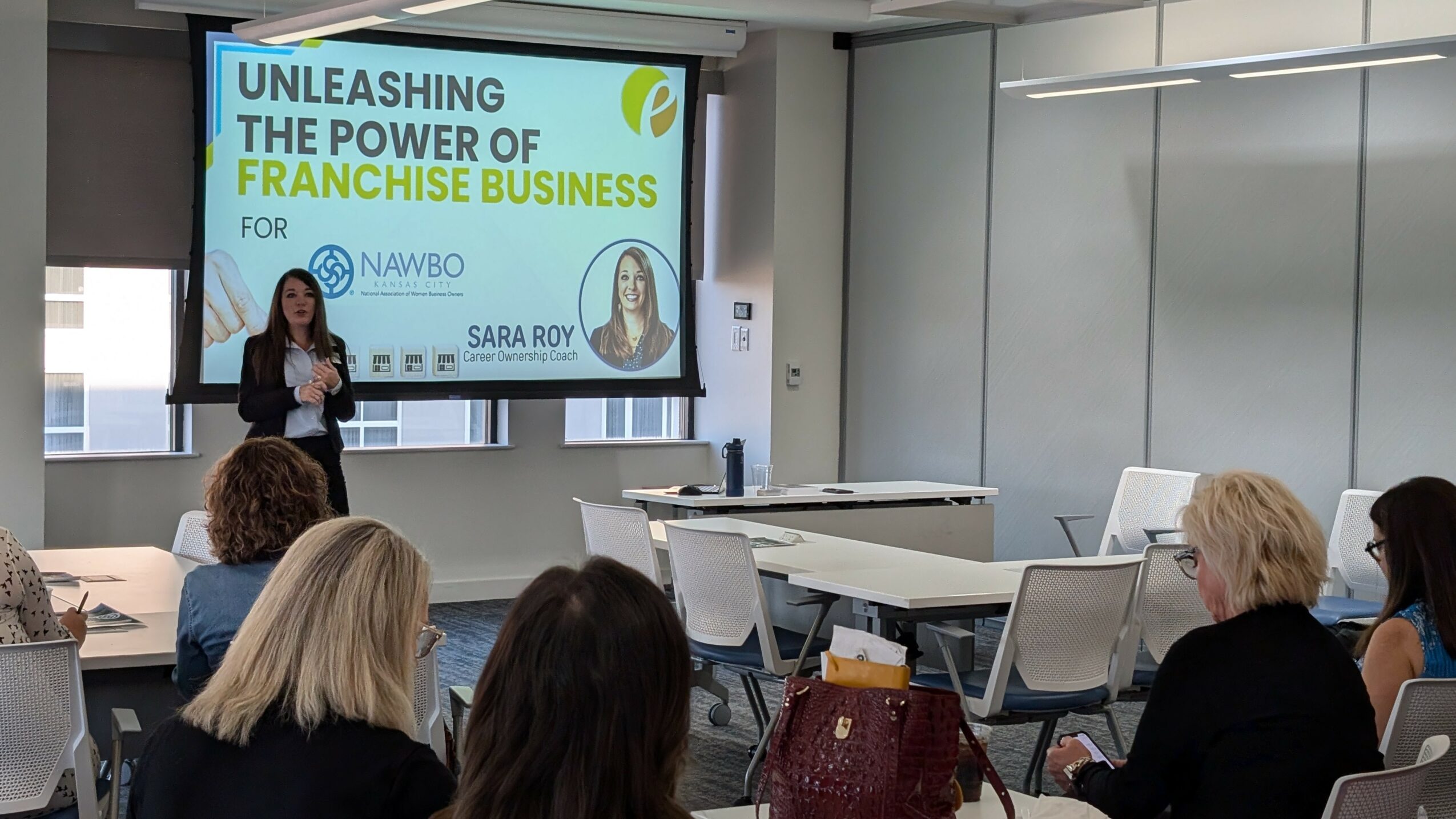 Woman presenting in a conference room with a slide titled 'Unleashing the Power of Franchise Business'. Audience seated and listening.