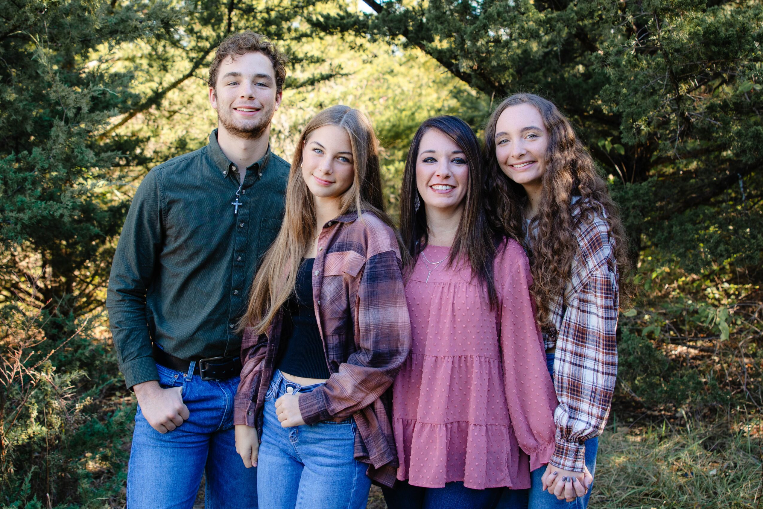 Four young women standing outdoors in front of trees, smiling at the camera.