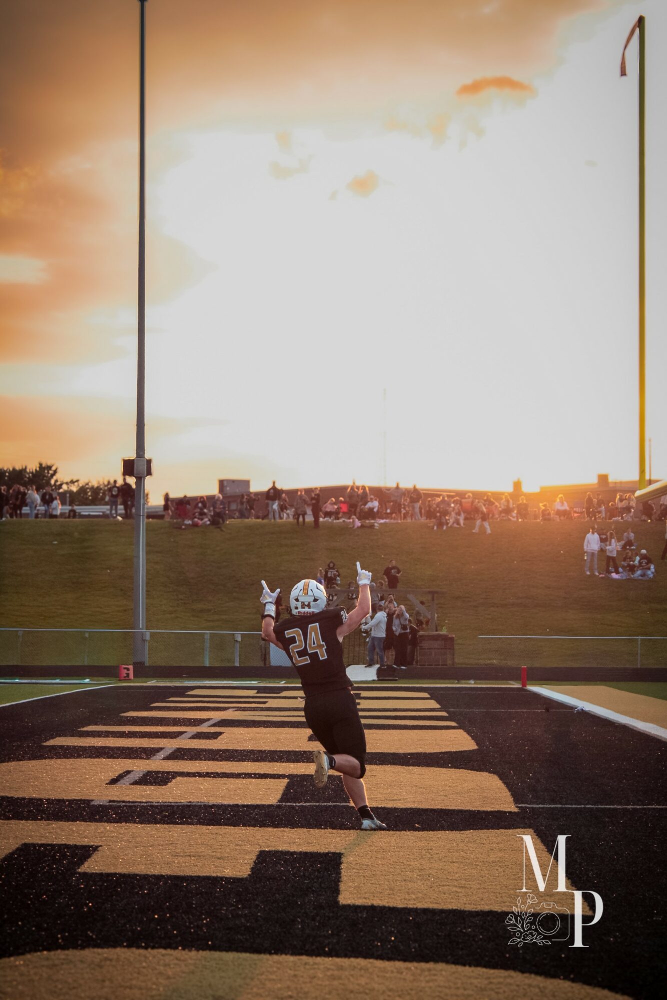 Football player wearing jersey number 24 catches the ball on a field during sunset, with spectators in the background.