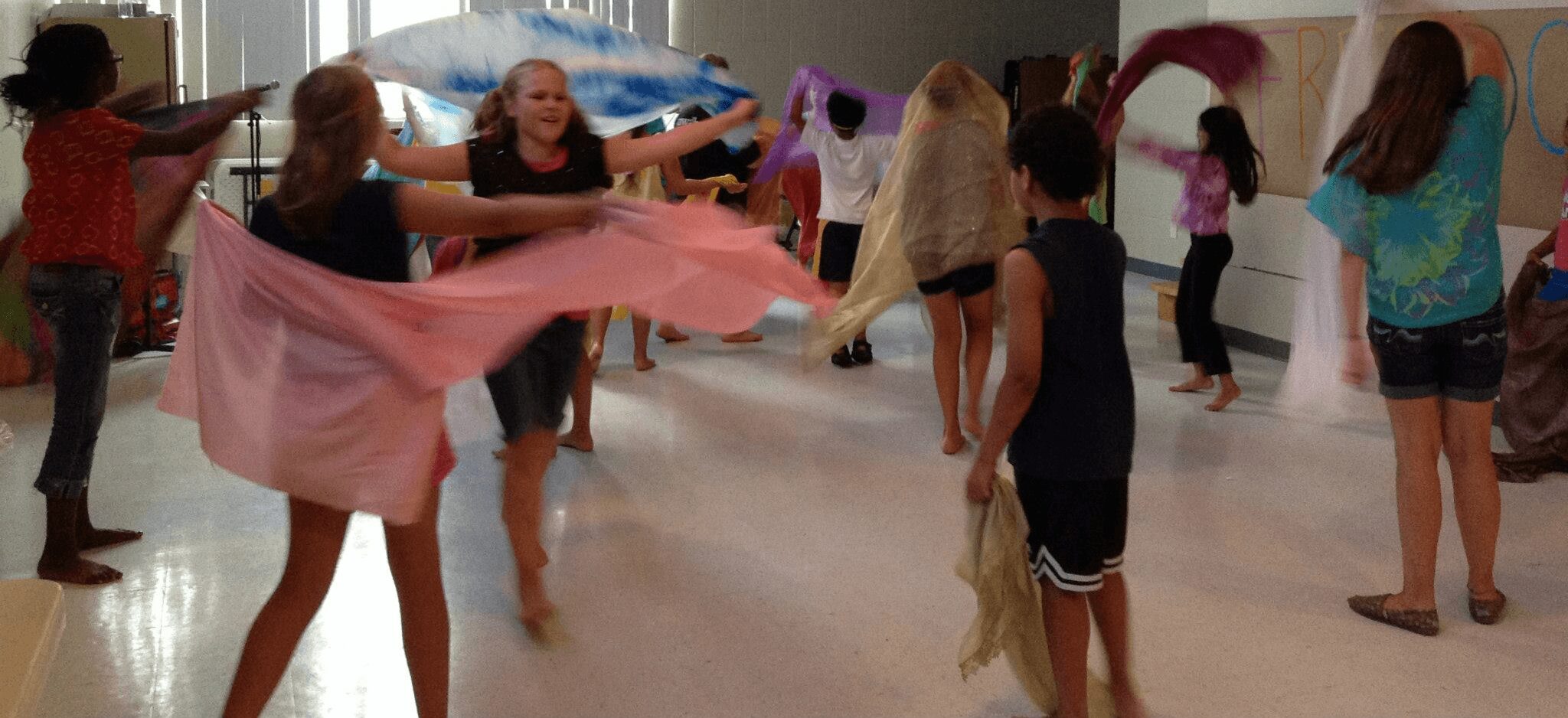 Group of people dancing and holding colorful scarves in a spacious room.