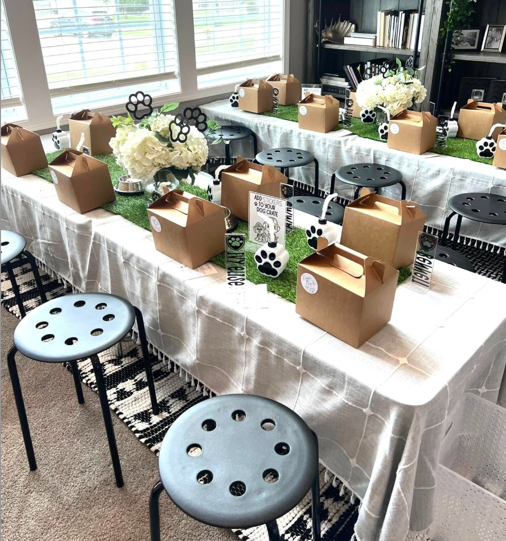 Table with brown boxes, white flowers, black chairs, and paw print decorations in a bright room.