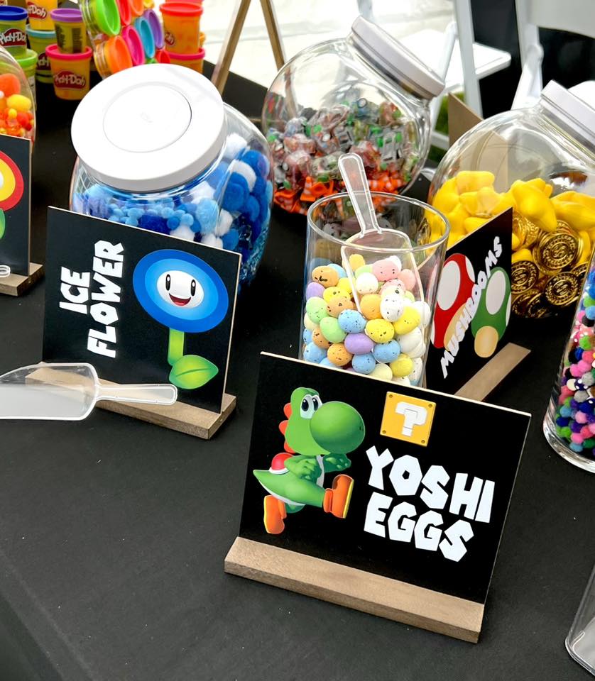 Display of colorful candies and toys with labels, including Yoshi Eggs with a cartoon dinosaur, on a black table.