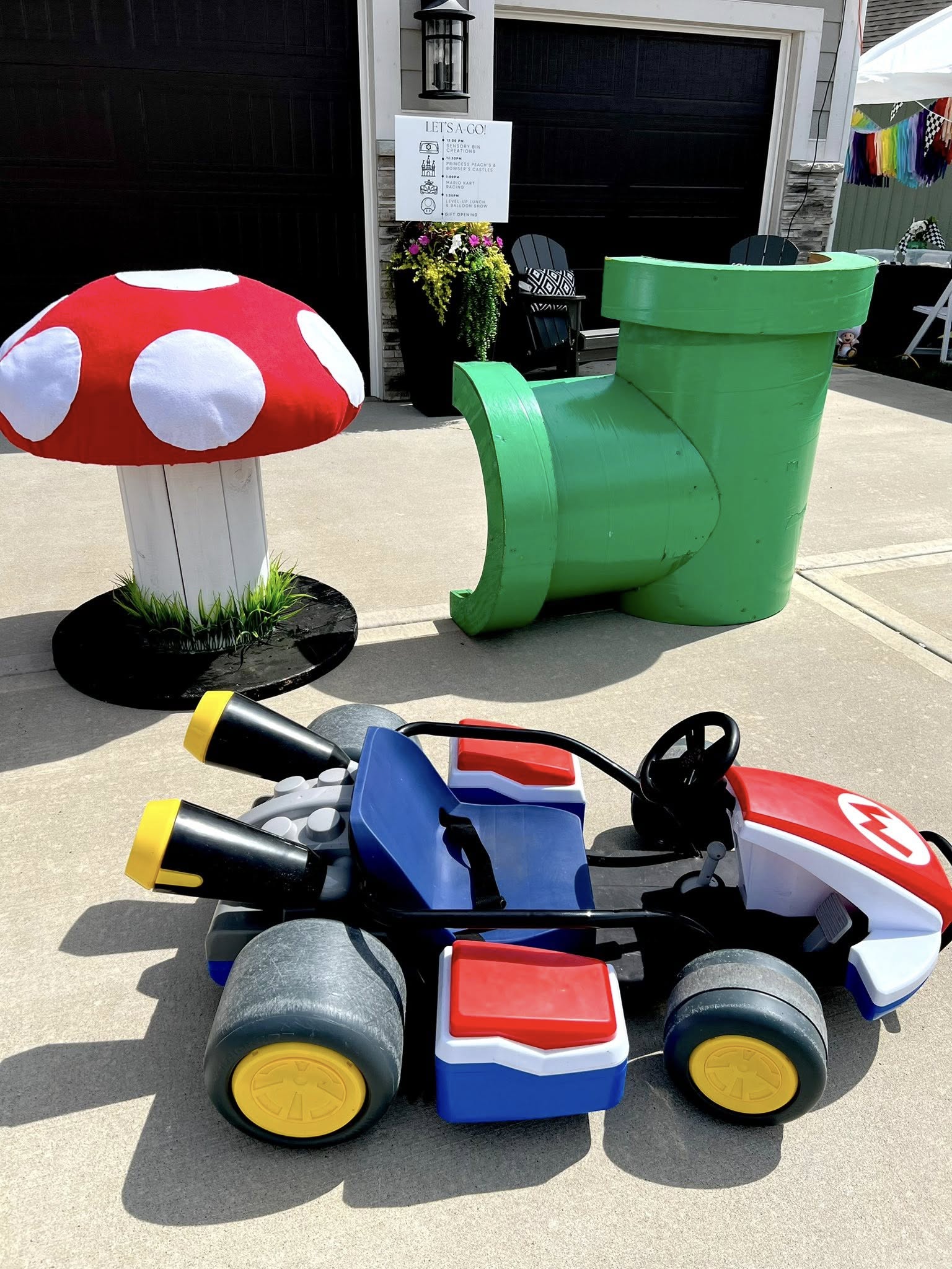 Colorful children's toy car, mushroom-shaped decoration, and large green chair outside on concrete surface.