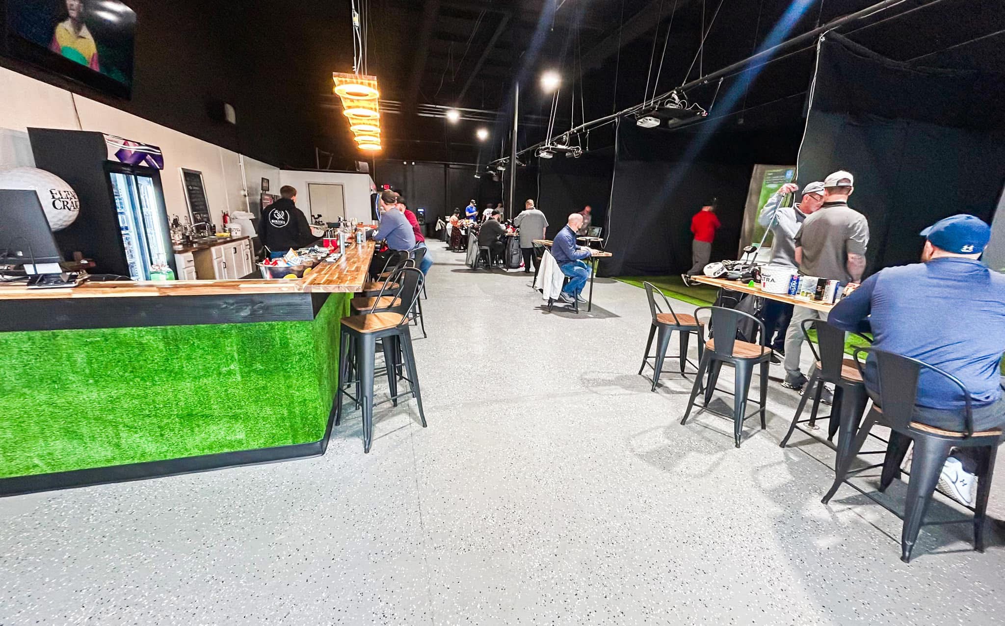 People sit at tables in a modern indoor space with a green counter and black ceiling.