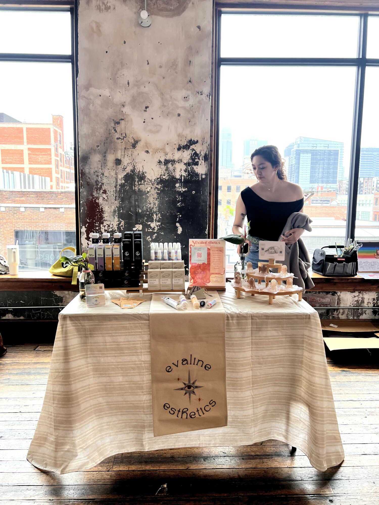 Woman standing behind a table with products in a room with large windows and city view.