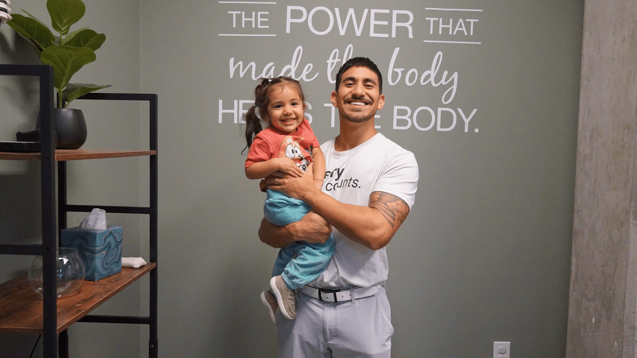 Man holding a young girl in front of a wall with motivational quote, smiling.