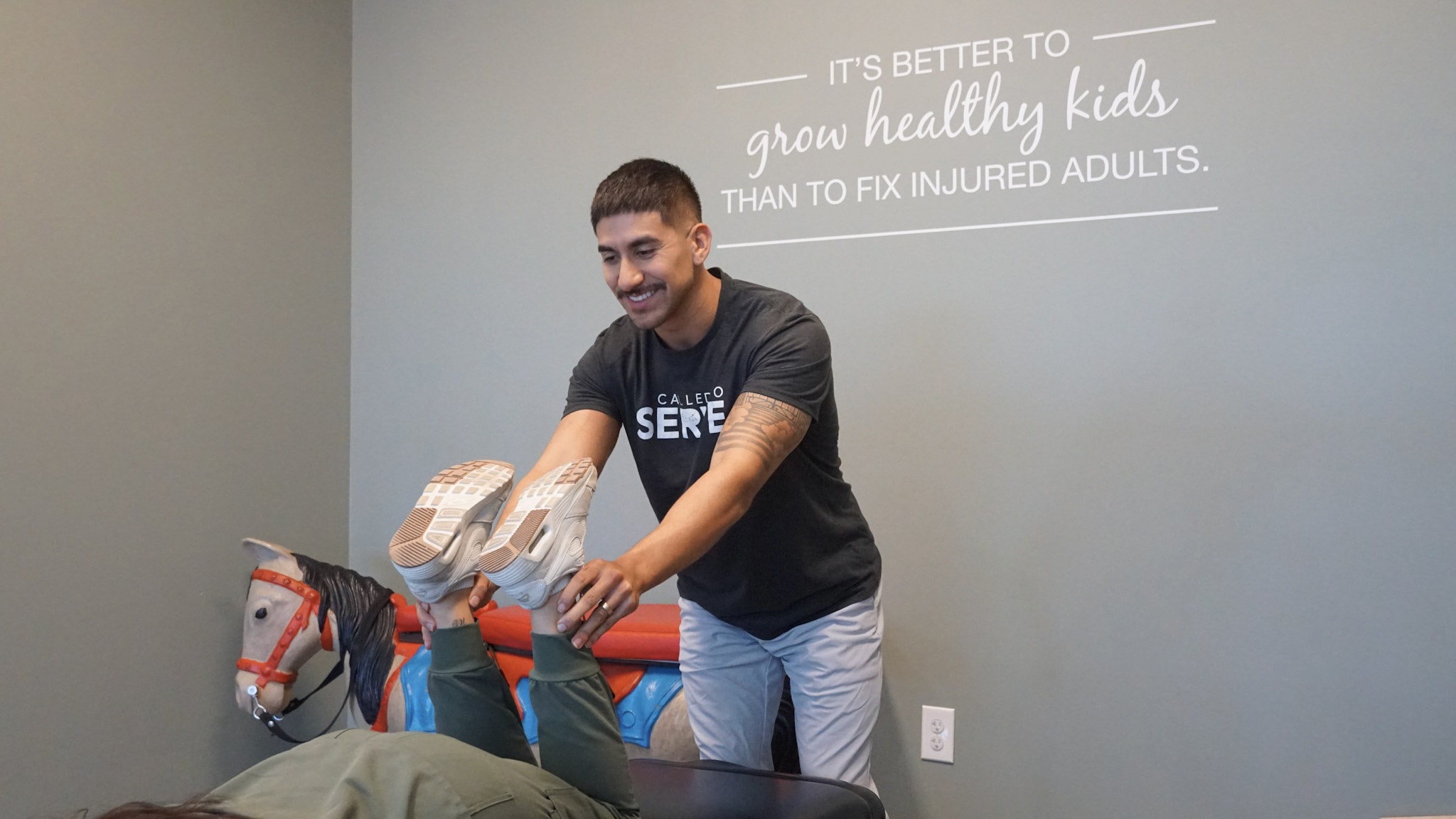 Young boy smiling and holding a pillow, standing in a room with a gray wall and a quote about healthy kids.