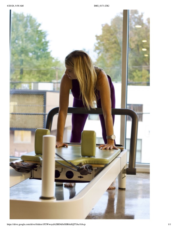 Person leaning forward on a treadmill in a gym with large windows and trees outside.