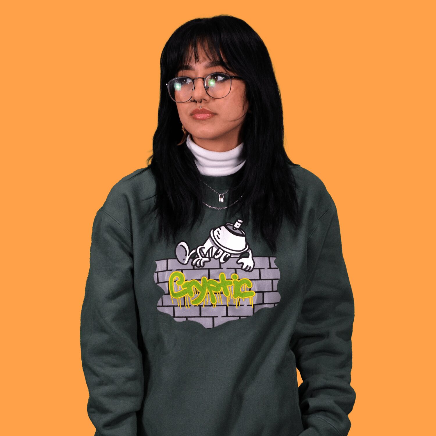 Young woman with black hair, glasses, wearing a gray sweatshirt with graffiti-style graphic, against orange background.