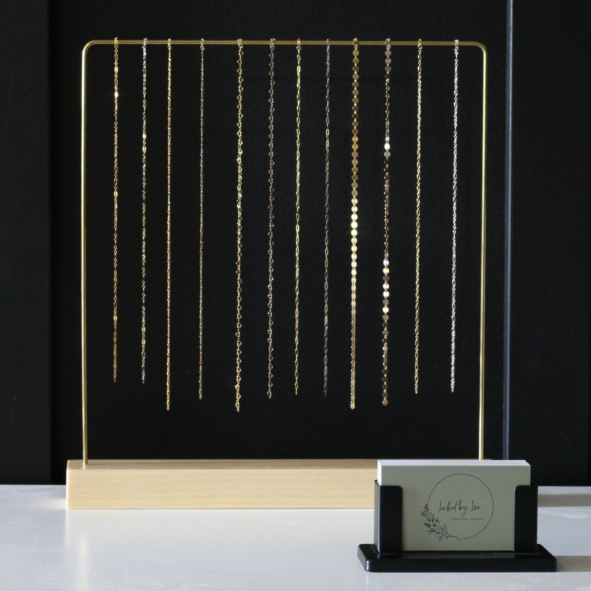 Display of hanging necklaces with various chain styles and lengths on a stand, with a small sign in front.