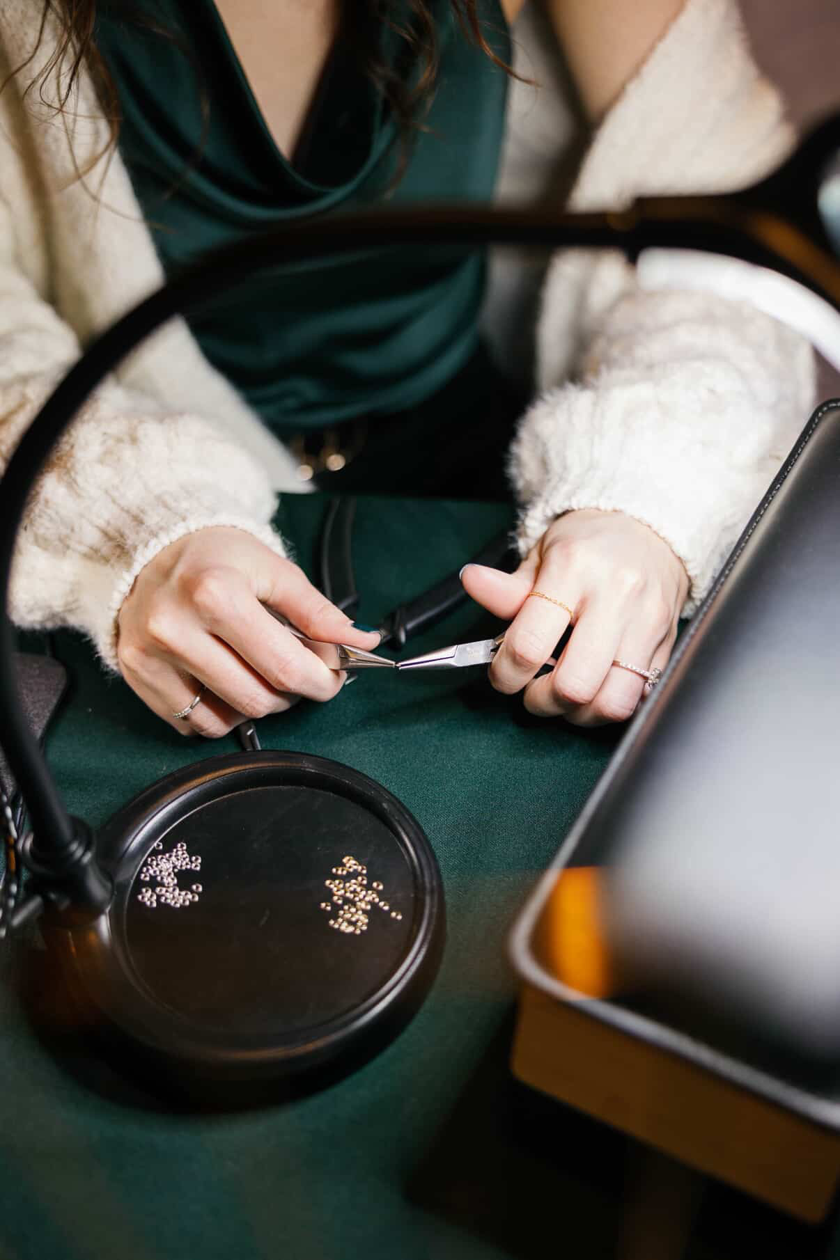 Person holding a pen and paper, wearing a white sweater and dark green top, sitting at a table.