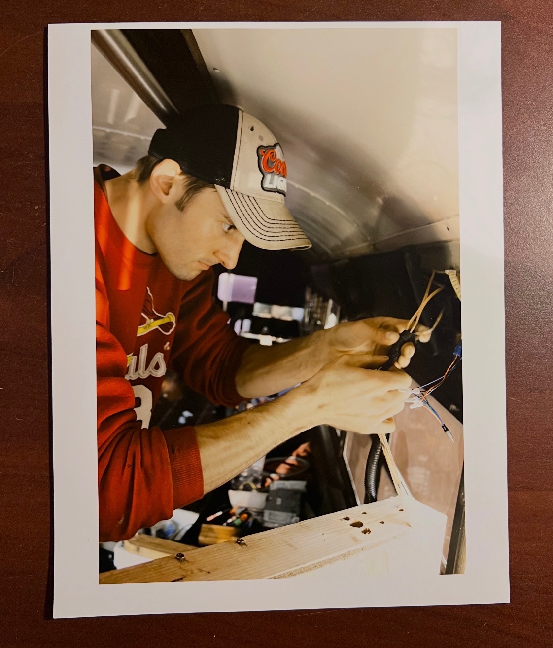 Young person working with tools inside a vehicle, wearing a baseball cap and red shirt, focused on task.