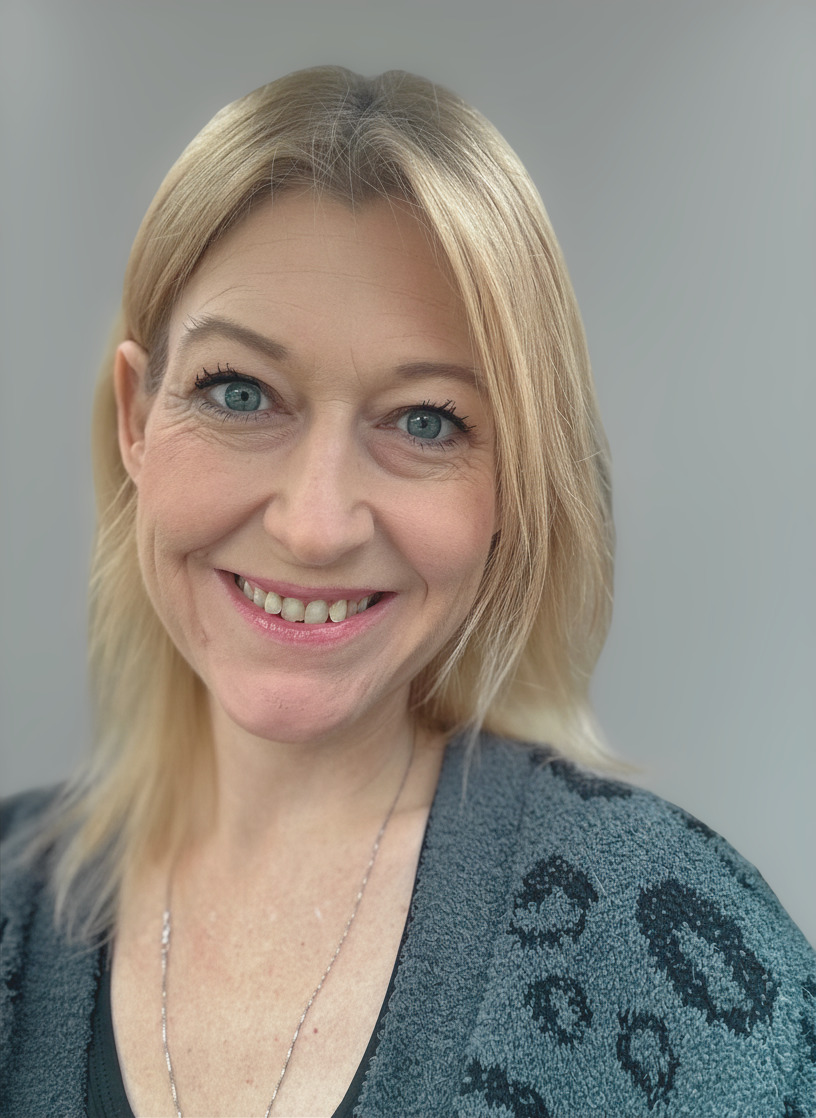 Woman with blonde hair smiling, wearing a gray top with a pattern, against a plain background.
