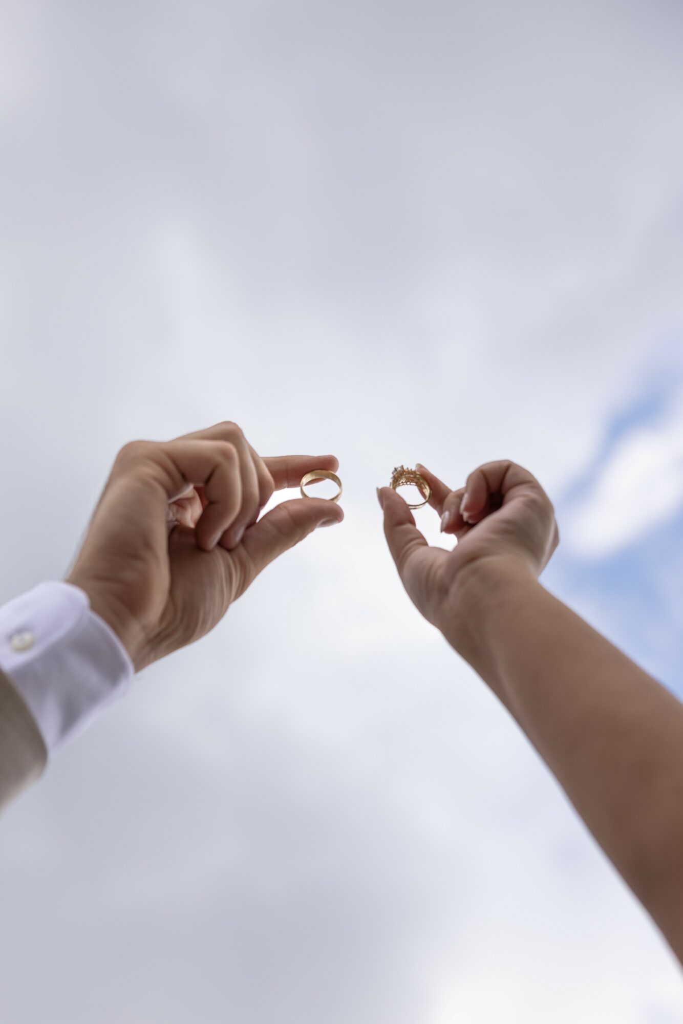 Two hands holding small objects against a cloudy sky background.