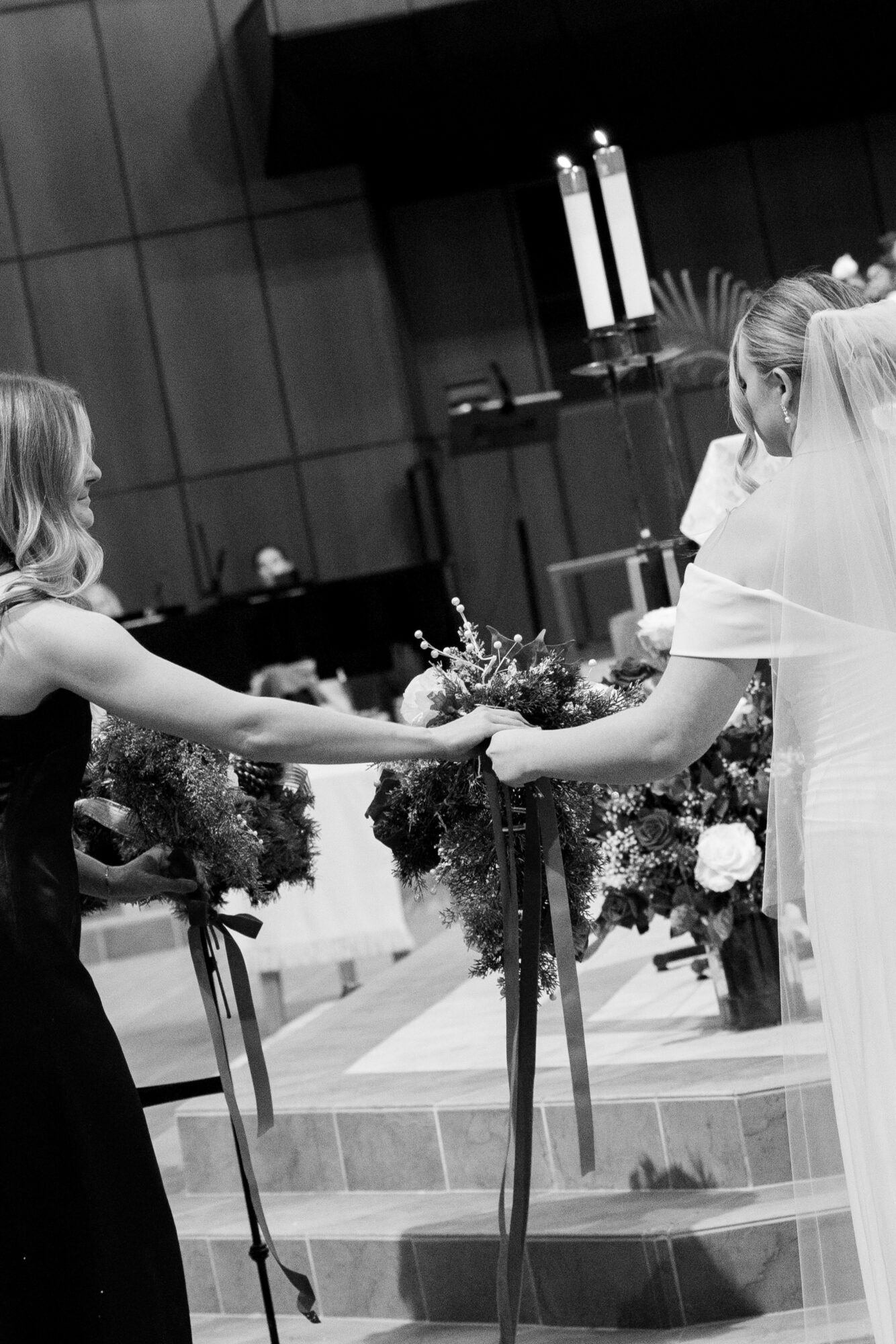 Two women holding hands during a wedding ceremony, with floral arrangements and candles in the background.
