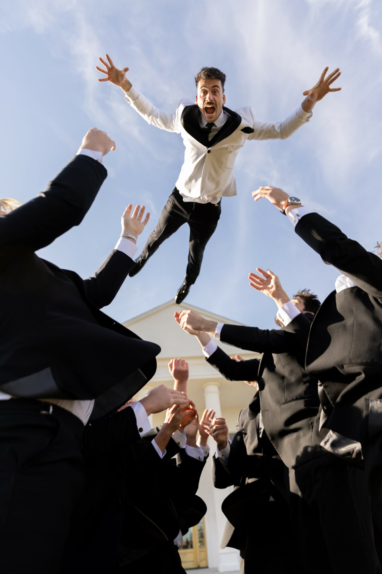 Man in formal attire falling from above with arms outstretched, surrounded by people reaching up towards him.