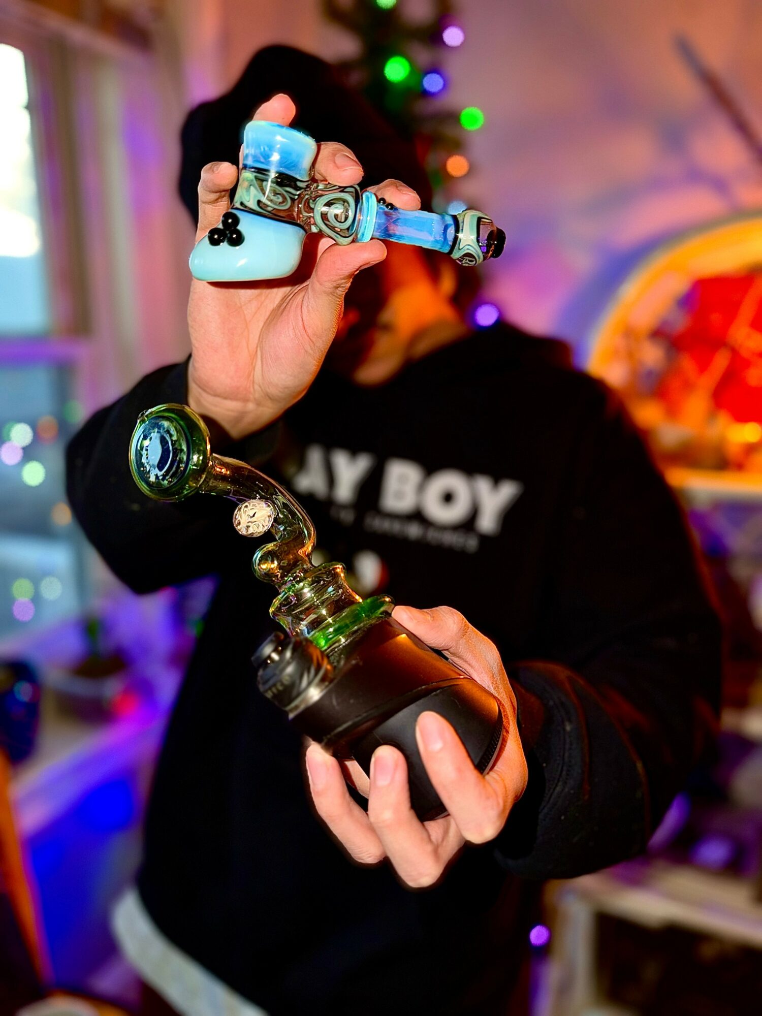 Person holding a colorful glass pipe and a black container in a room with colorful lights.
