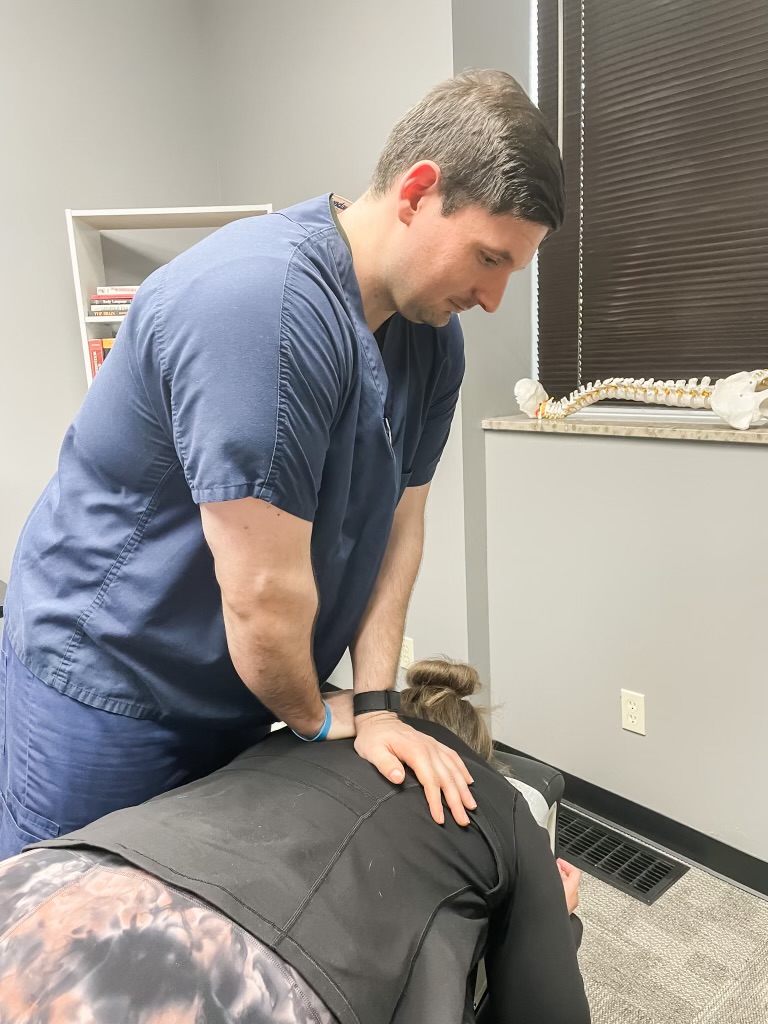 Person in blue scrubs providing a massage or therapy to a person lying face down on a table.