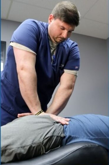 Male healthcare professional performing a procedure on a patient's back in a clinical setting.