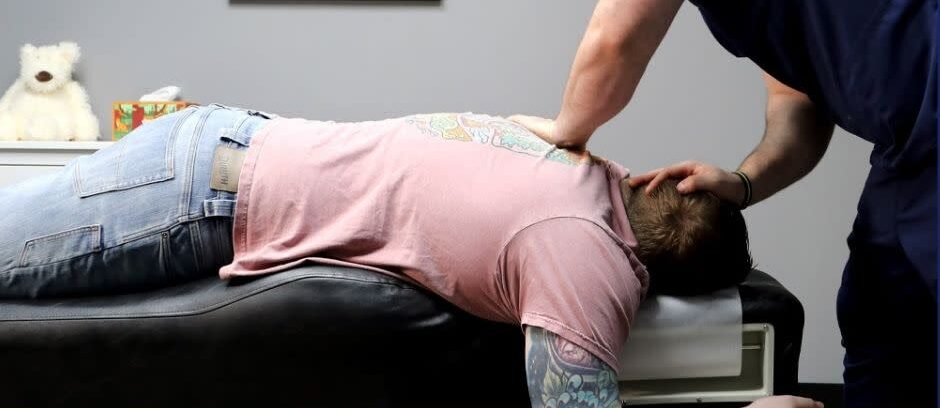 Person lying face down on a table receiving a neck or back treatment from a professional.
