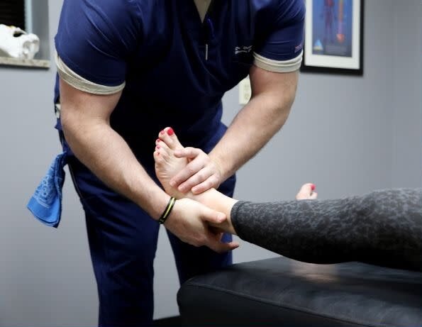 Therapist holds patient's foot during a physical therapy session in a clinical room.