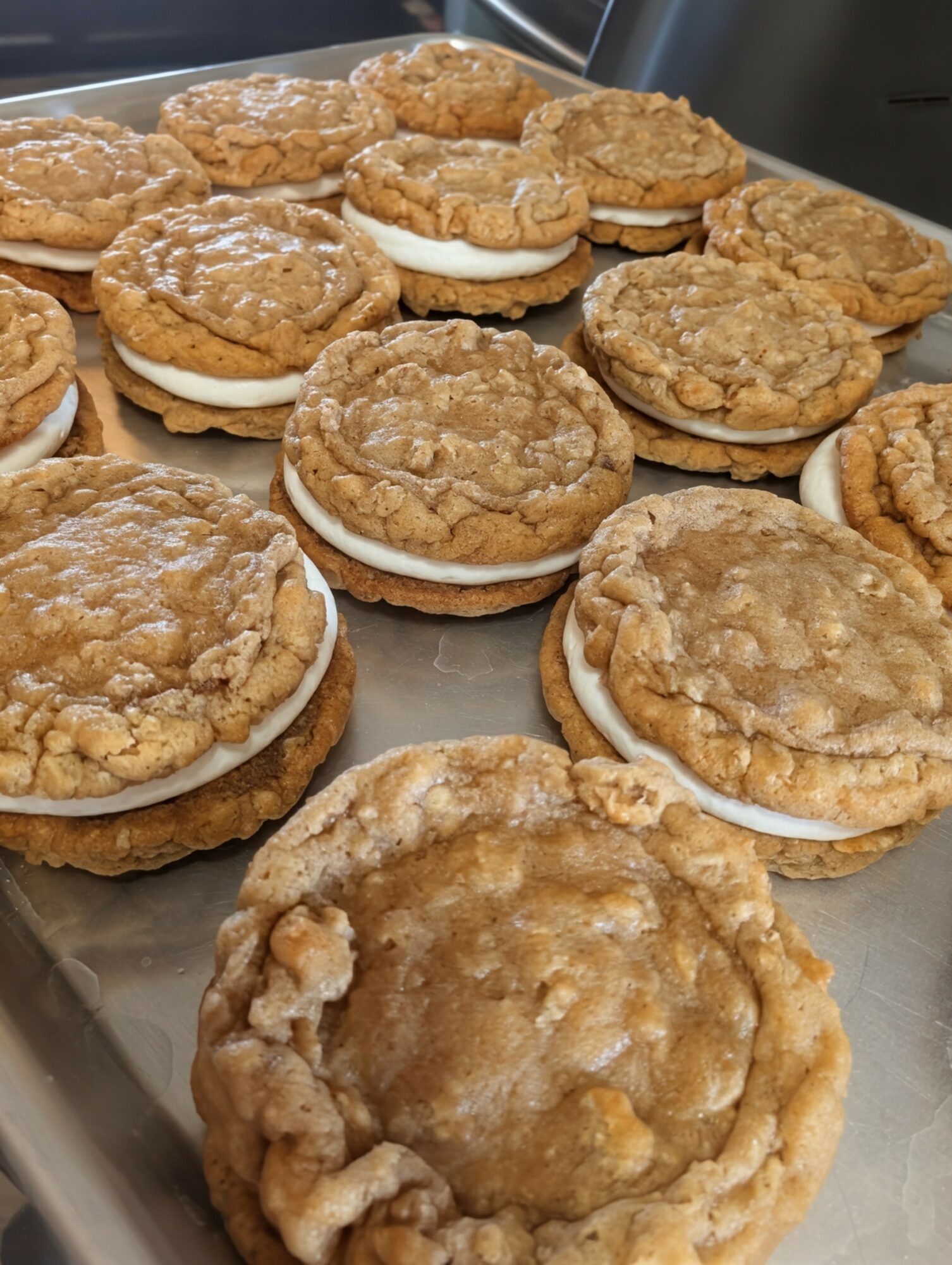 Several cookies with a crumbly topping and white filling on a metal tray.
