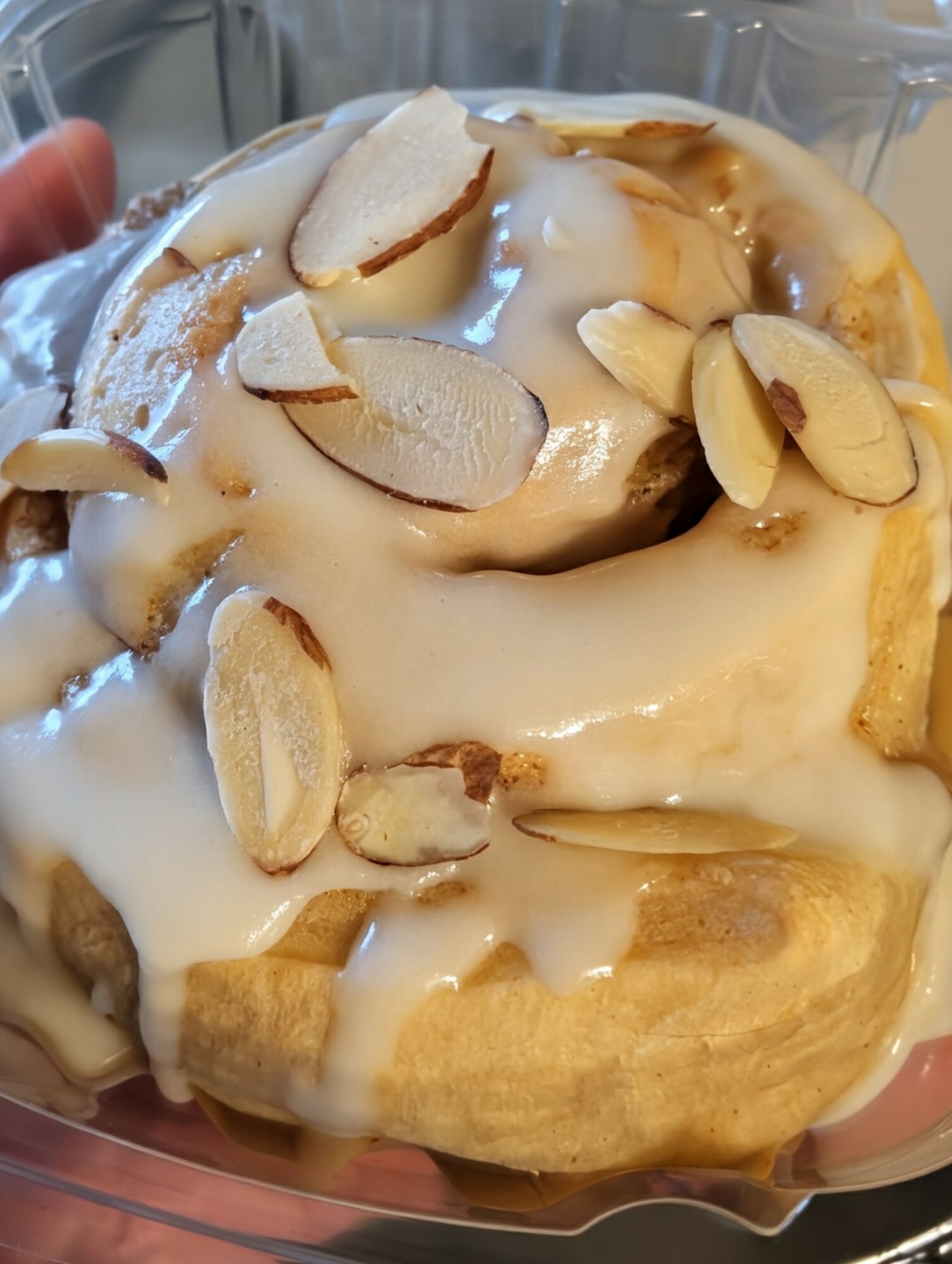 Pastry topped with white icing and sliced almonds, in a clear container.