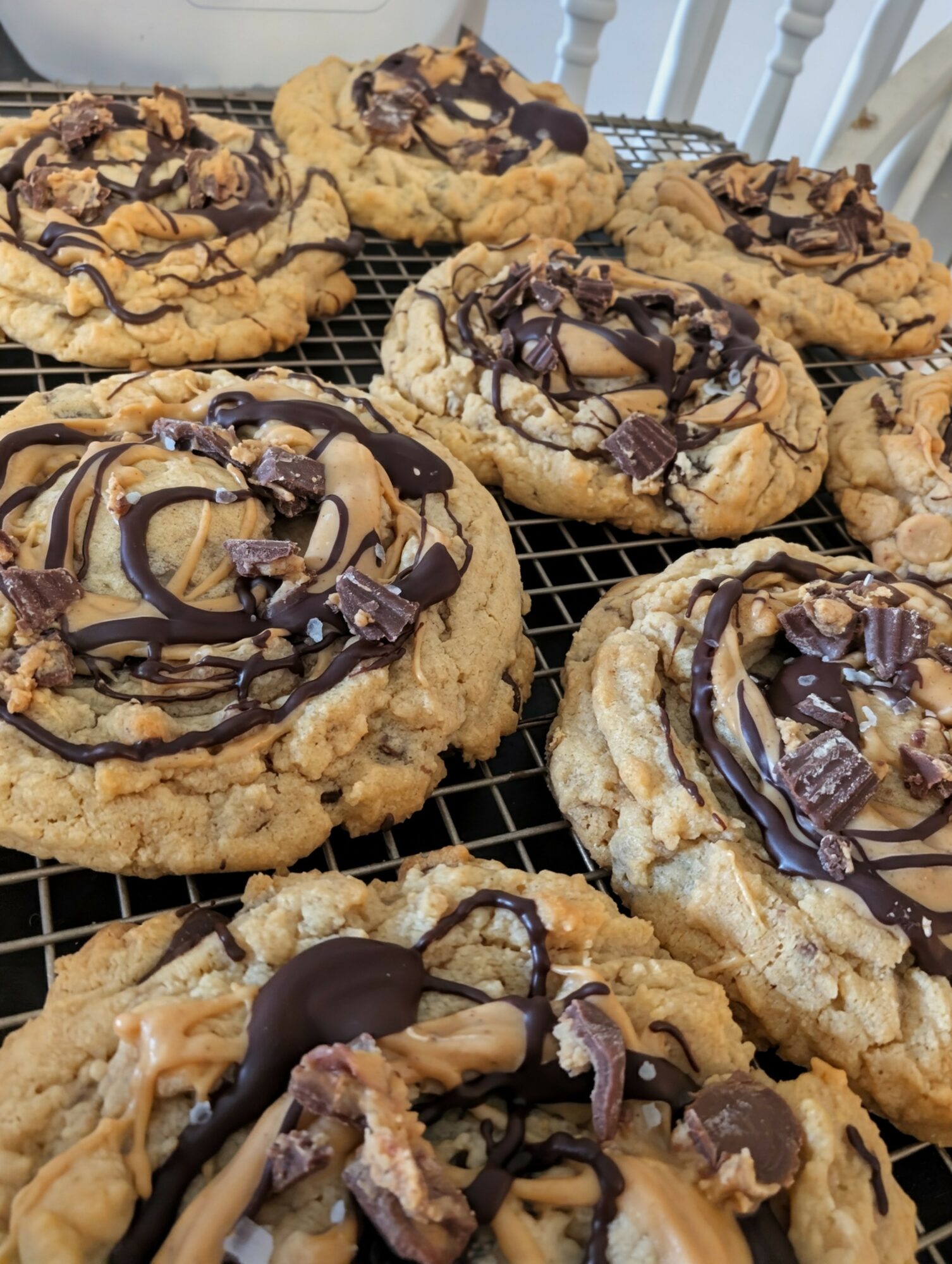 Several large cookies with chocolate drizzle and chopped chocolate pieces on a wire rack.