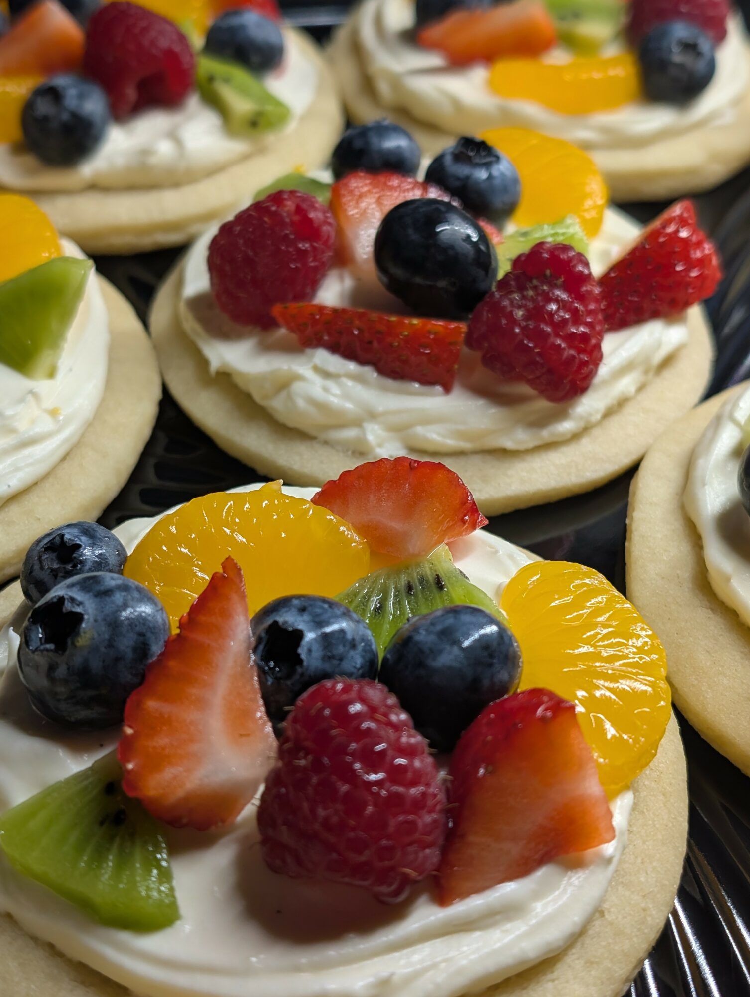 Assorted fruit-topped mini pavlovas with whipped cream, including strawberries, blueberries, raspberries, kiwi, and orange slices.