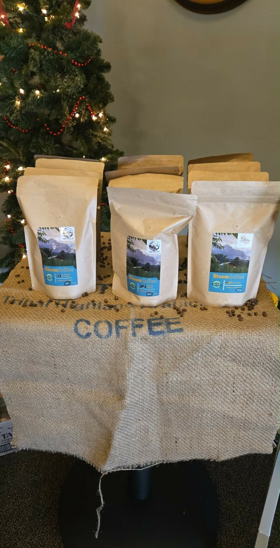 Four white coffee bags on a table with a Christmas tree in the background.