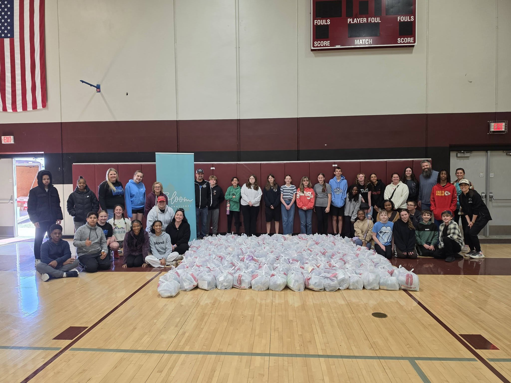Group of people standing and sitting in a gymnasium with a large pile of white objects in front.