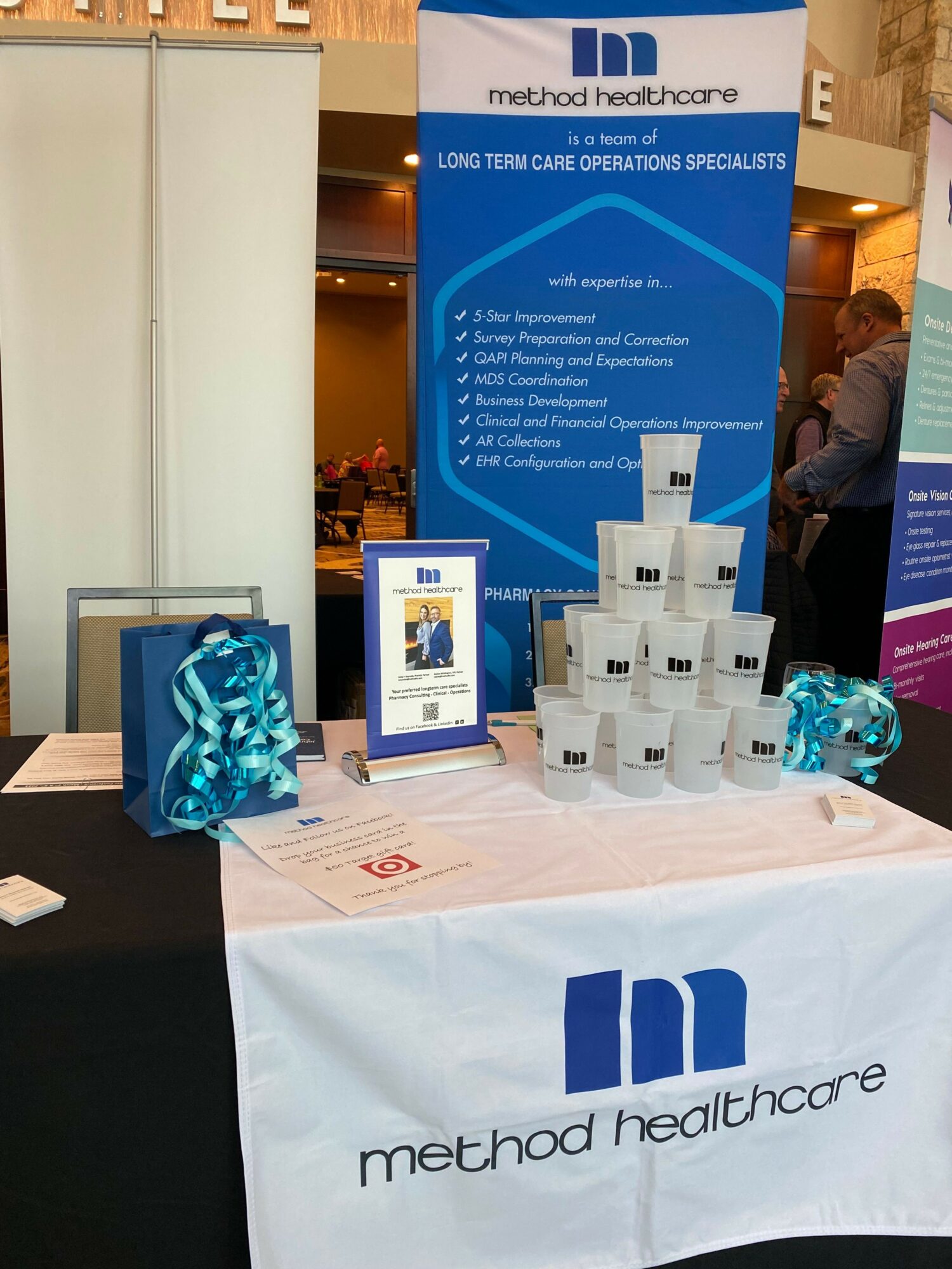 Method Healthcare promotional display with stacked white boxes, a blue banner, and a tablecloth with company logo.