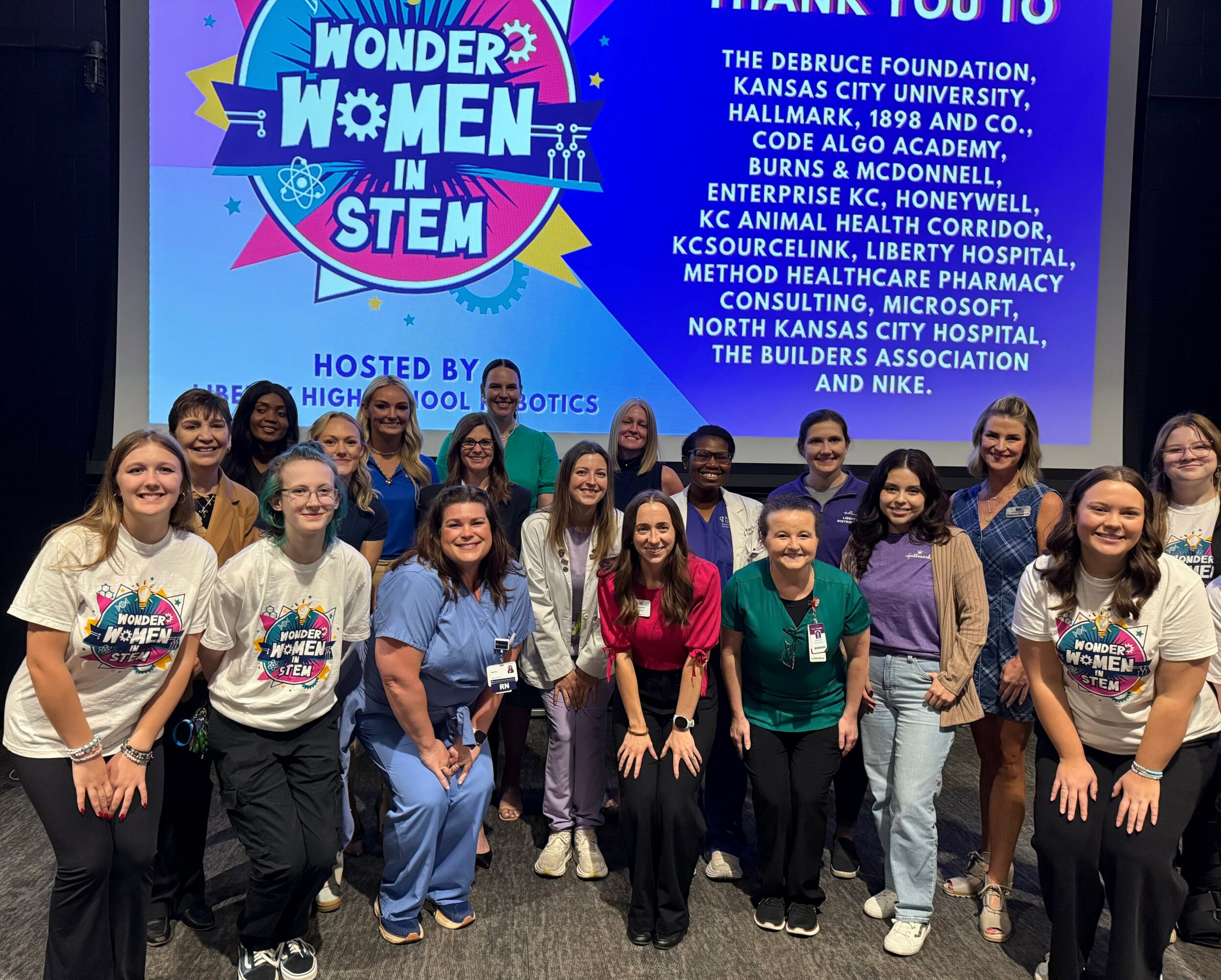 Group of children and adults standing in front of a large screen with event information and logo.