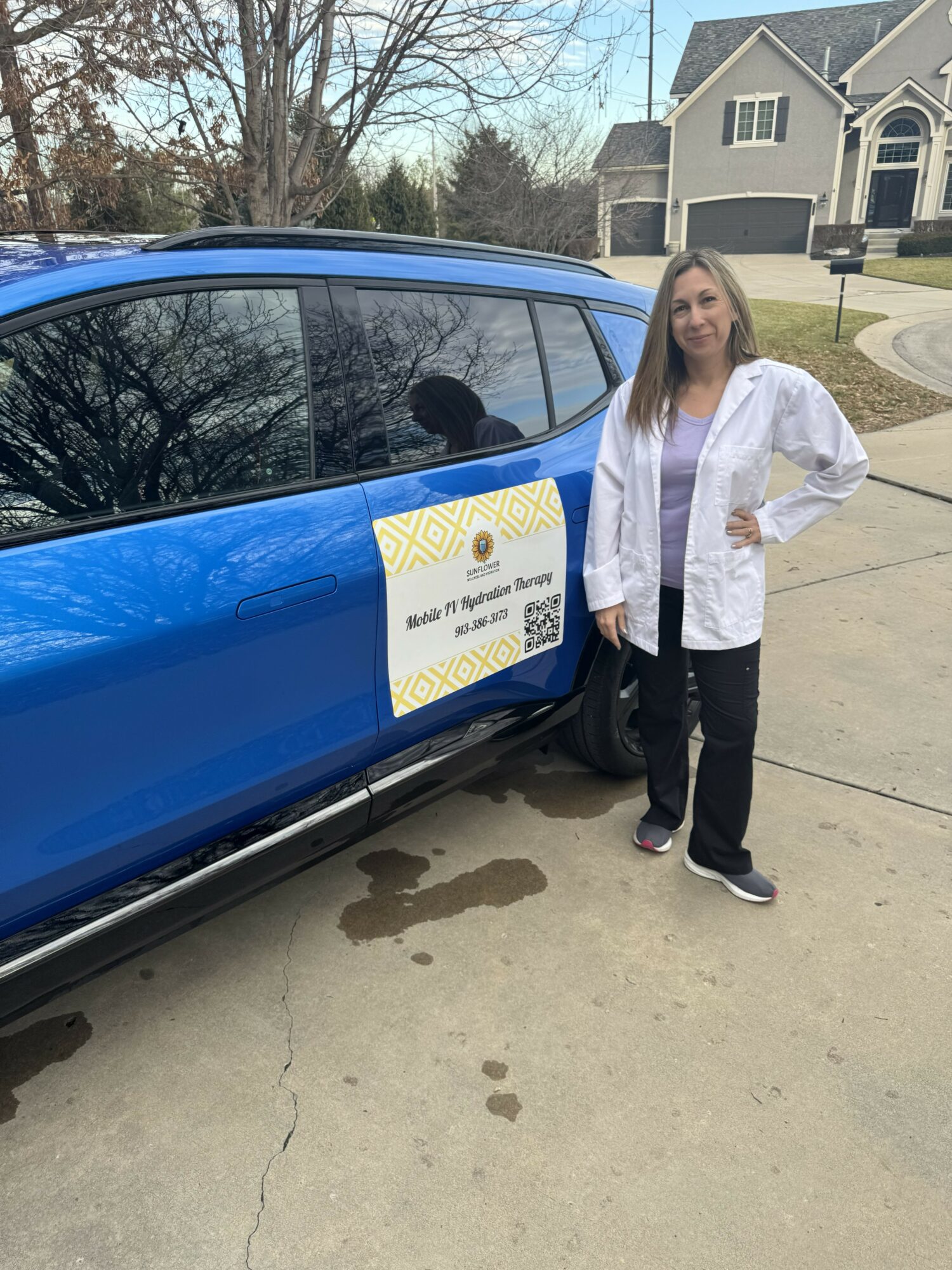 Woman standing next to a blue car with a sign on the door, in a residential neighborhood.