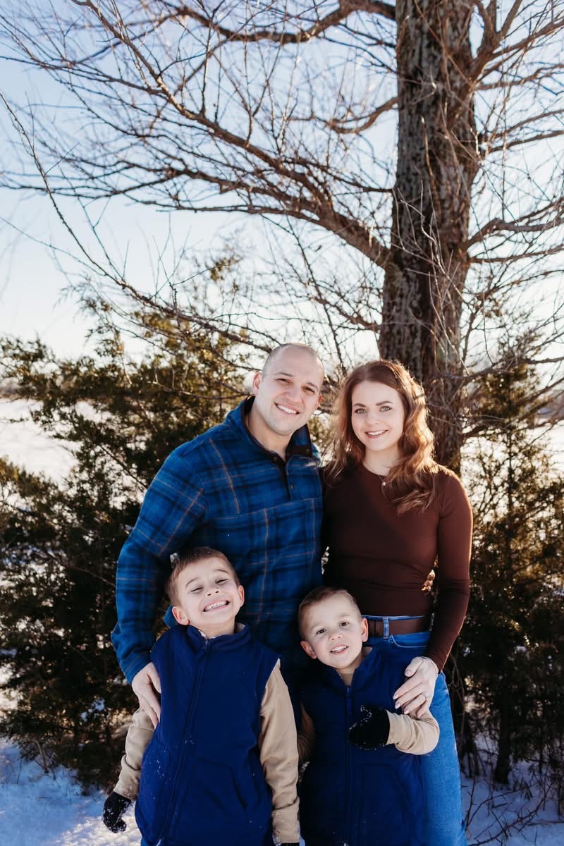 Two adults and two children standing outdoors in winter, smiling, with trees and snow in background.