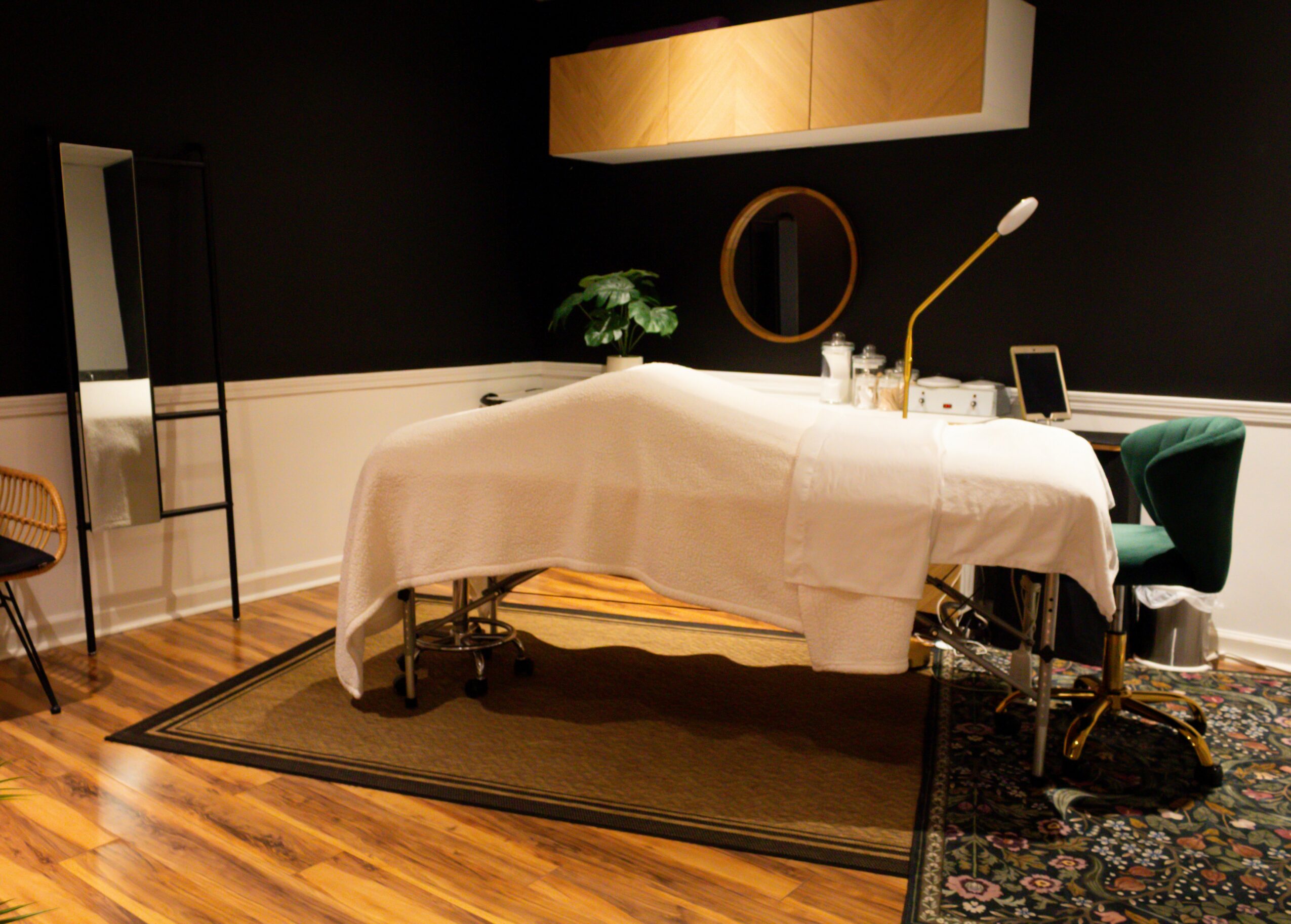Massage table covered with white sheet in a room with dark walls, wooden floor, and decorative items.